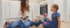 Una donna e un bambino giocano con peluche sul pavimento di una cucina moderna di Nolte Kitchen.