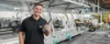 Un uomo sorridente accanto a una macchina in un moderno impianto di produzione.