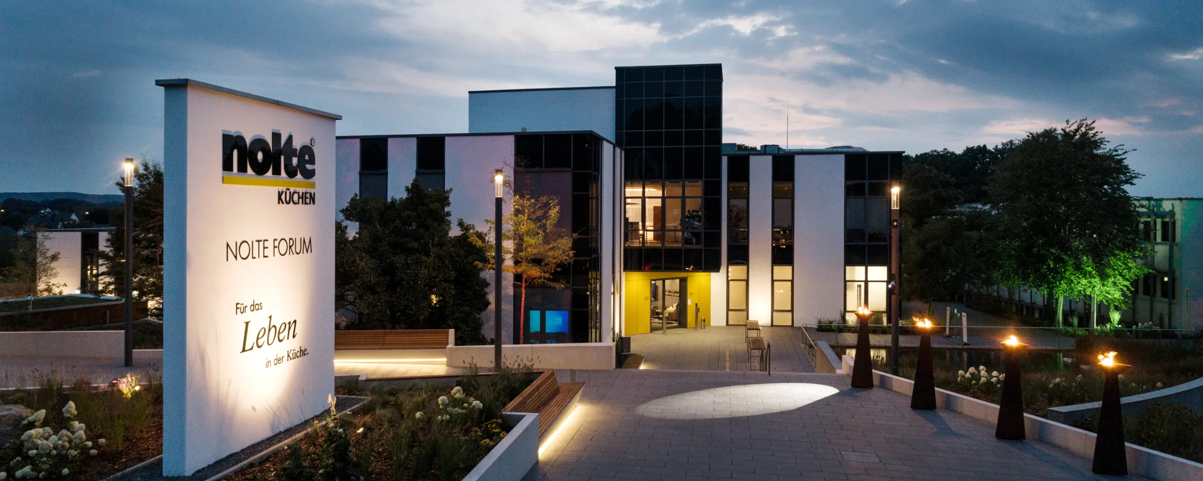 Edificio moderno al crepuscolo con insegna illuminata di Nolte Kitchen in primo piano.
