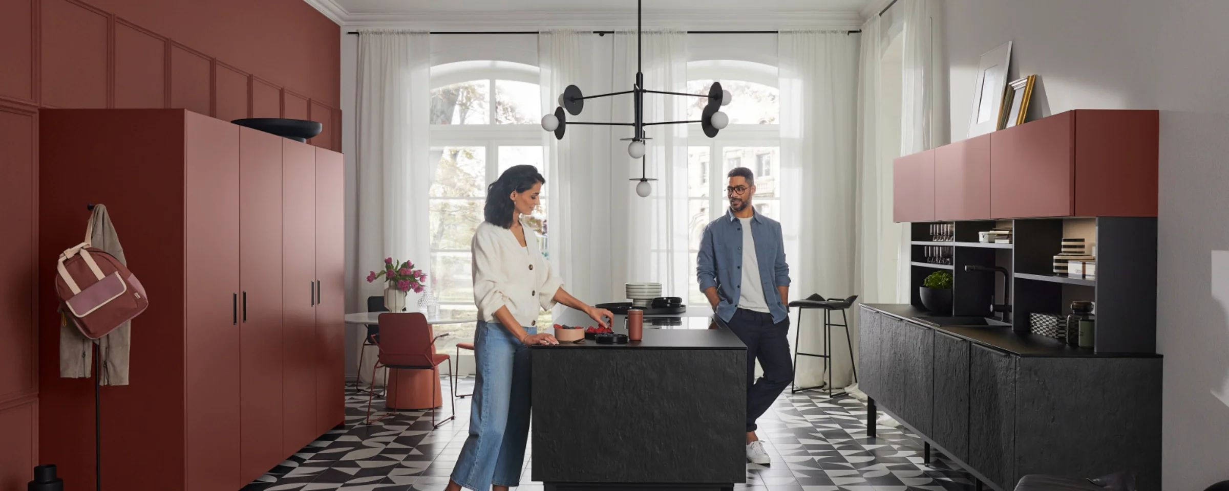 Cucina moderna Nolte con due persone, pavimento geometrico e armadi rossi.