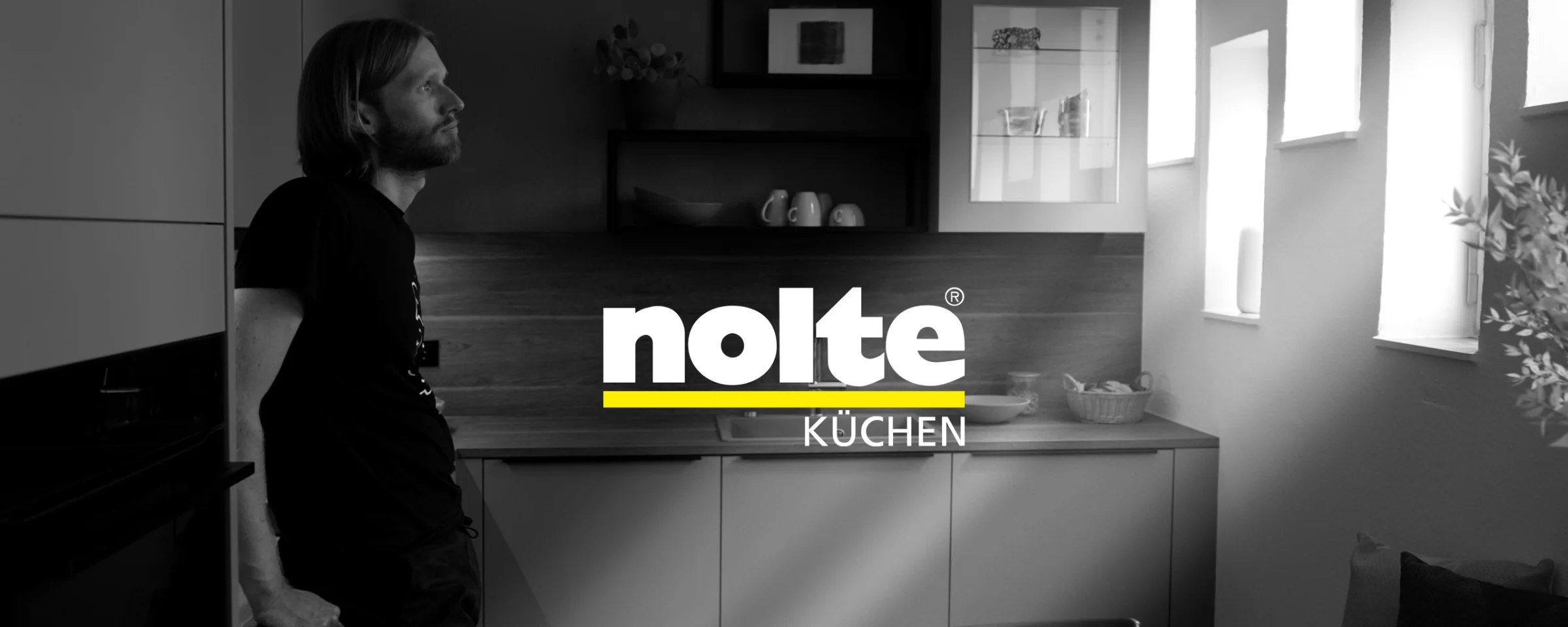 A man leans against the countertop in a modern Nolte kitchen.