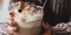 Persona con tazza di cioccolata calda, panna montata e bastoncino di cannella.