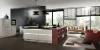 Moderna Nolte cucina con il frontale lucido NOVA LACK Platingrau. La cucina a isola senza maniglie colpisce per le linee chiare, un ampio piano di lavoro con piano cottura integrato e uno spazio aperto a scaffale in caldo rosso bruno. L'ambiente appare aperto e inondato di luce grazie a finestre a tutta altezza e un arredo elegante con un'accogliente area salotto in stile soggiorno.