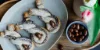 Tre dolci al cioccolato su un piatto con mandorle, accanto un vaso di fiori.