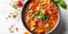 Un piatto di zuppa di lenticchie, guarnito con erbe fresche, circondato da pomodori e spezie.
