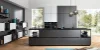 Moderna cucina Nolte con la frontale FERRO in acciaio blu e pensili a contrasto in SOFT LACK Arcticweiß softmatt. La cucina con isola senza maniglie colpisce per linee chiare, scaffali aperti e soluzioni di stivaggio integrate. Ampie finestre assicurano un ambiente luminoso che sottolinea con stile il carattere industriale delle superfici in acciaio blu.