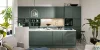 Moderna cucina Nolte con una combinazione di frontali FRAME LACK e SOFT LACK in Black Green softmatt, isola di cottura con design a cornice e piano di lavoro chiaro in Beton Weiß, combinata con accogliente area soggiorno.