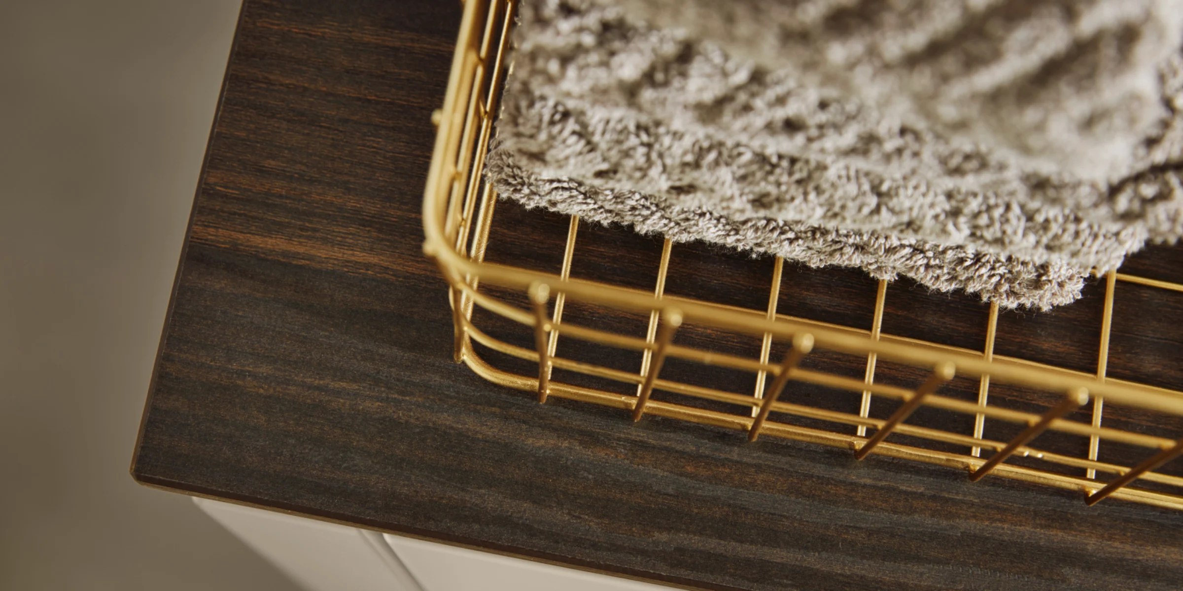 Cesto dorato con asciugamani su uno scaffale in legno scuro di Nolte Living.