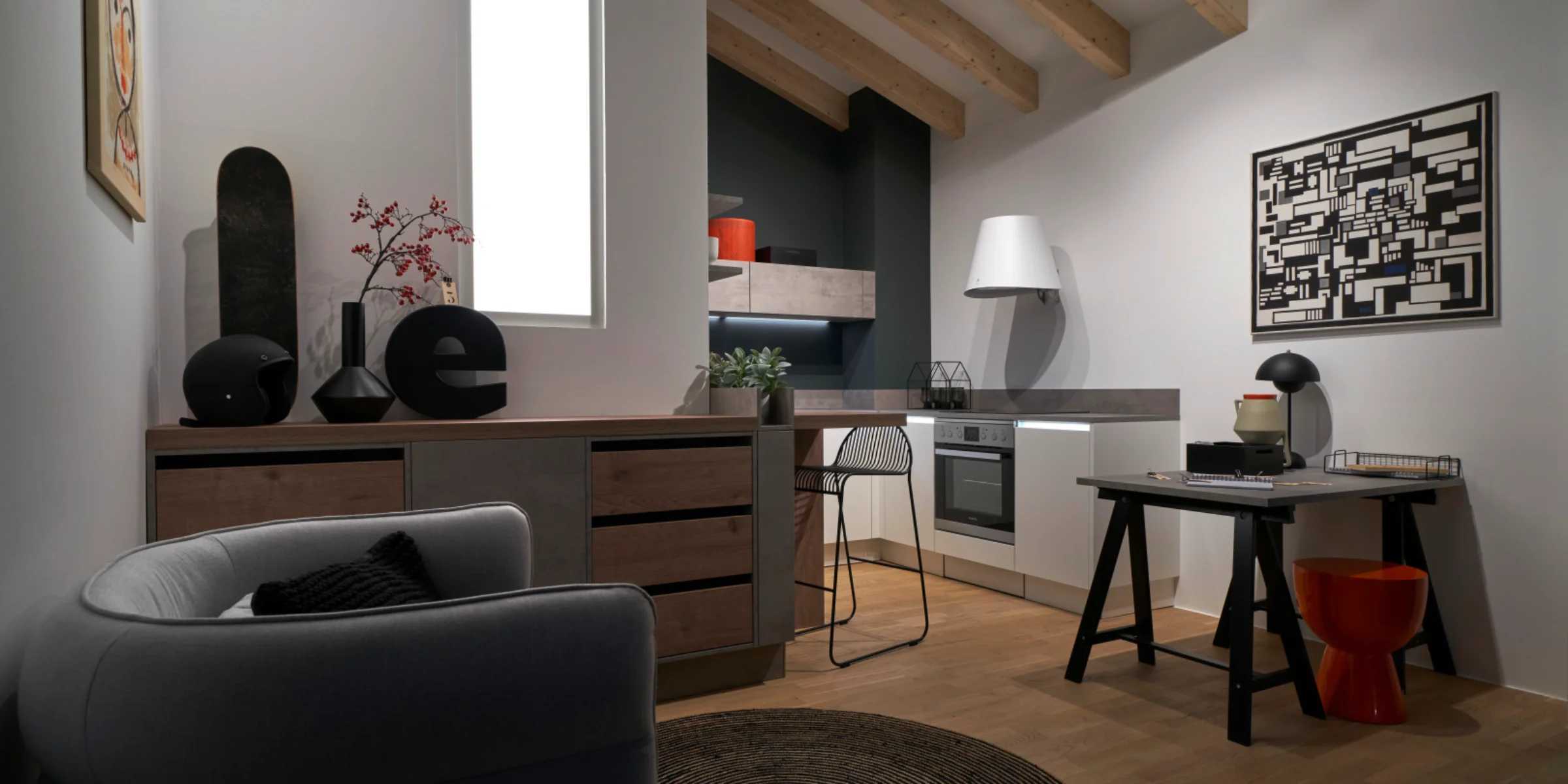 Stilvolmente arredata cucina tiny sotto le falde del tetto con il programma di frontali FEEL in bianco opaco e piano di lavoro STONE in cemento a contrasto. Progettazione compatta con area living e lavorativa in un unico spazio.
