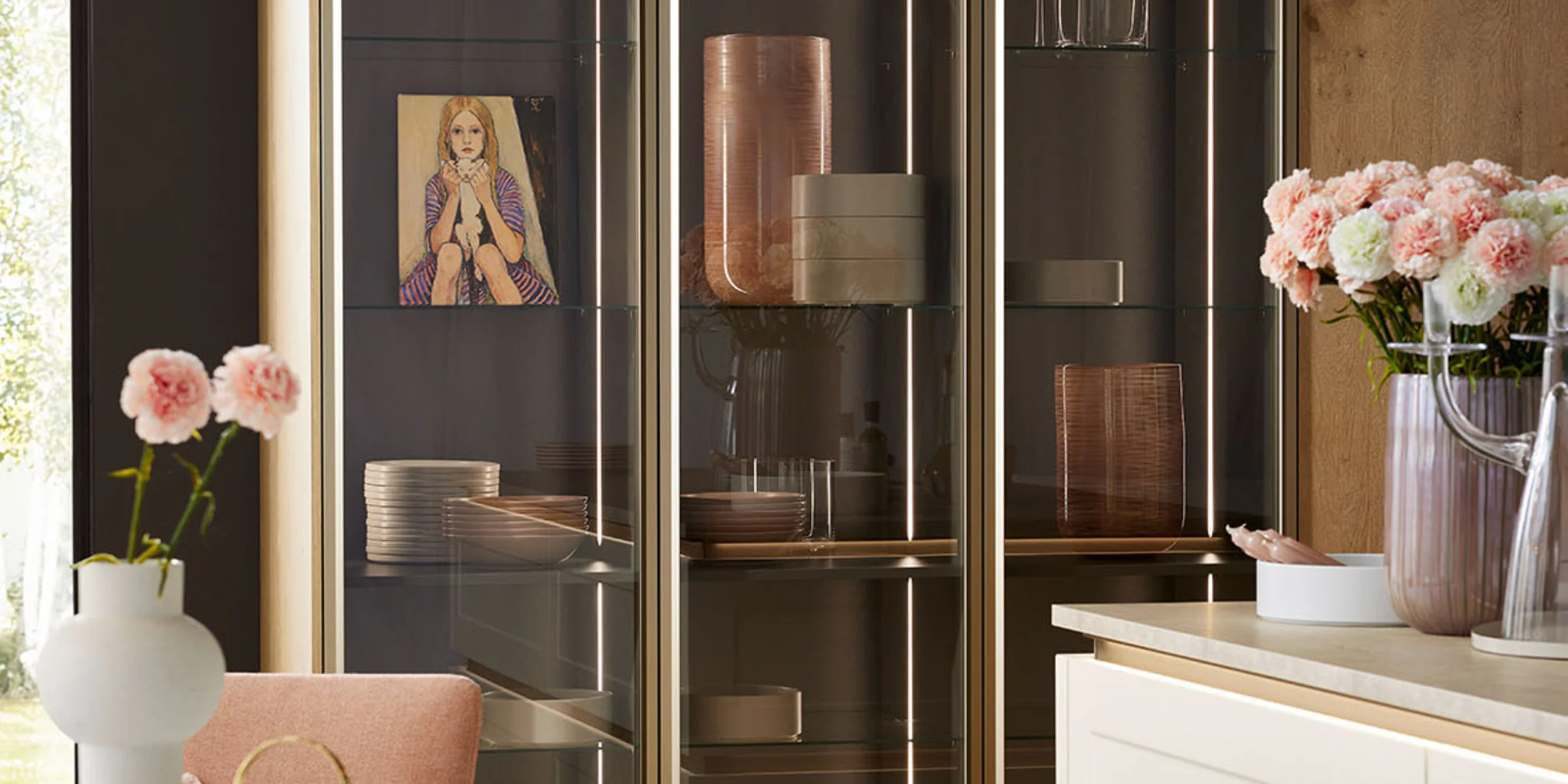 Cucina moderna con vetrine in vetro e frontali in legno, decorata con fiori e arte, di Nolte Kitchen.