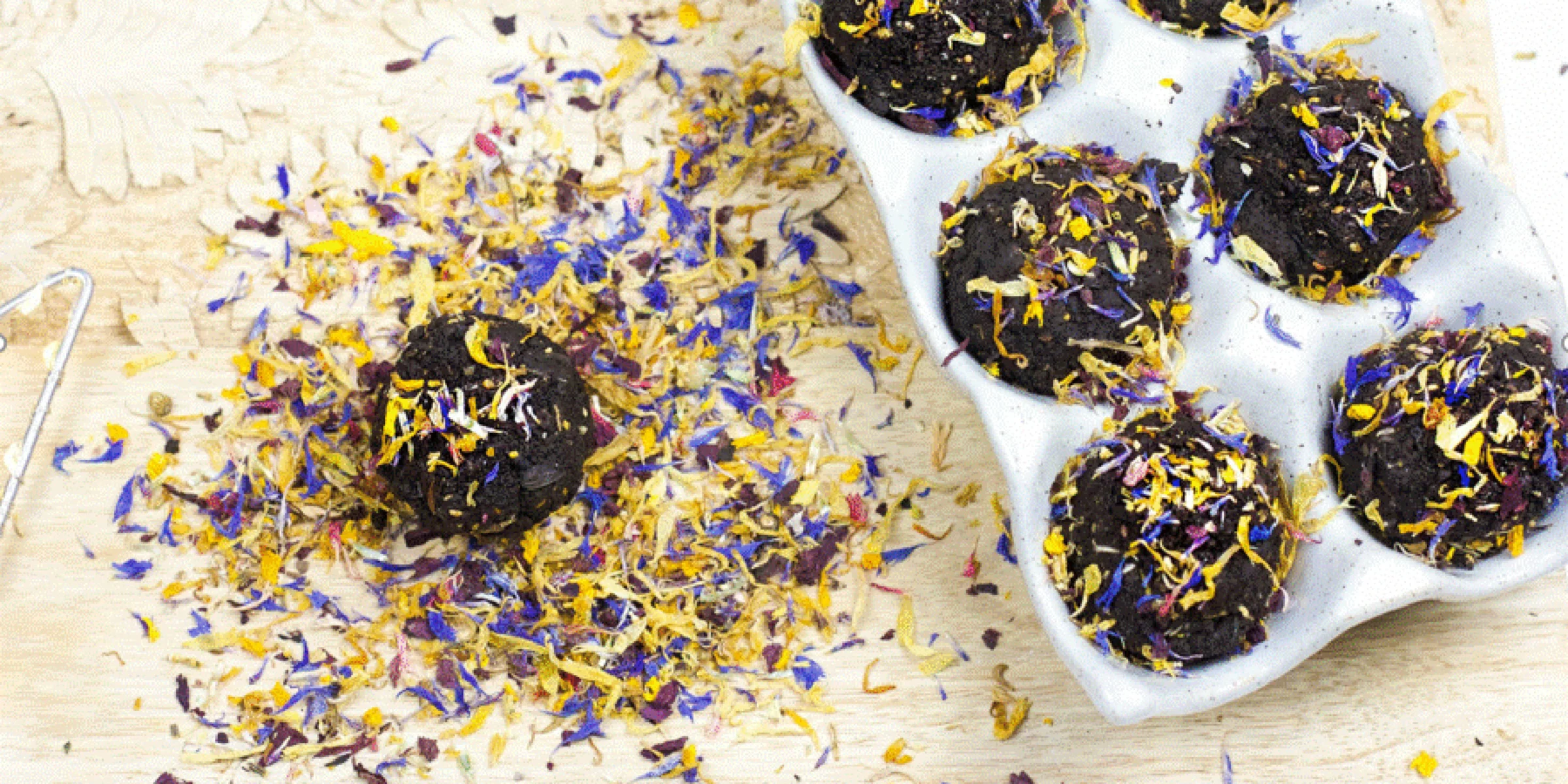 Una confezione di muffin al cioccolato decorati con fiori secchi su un tagliere di legno.