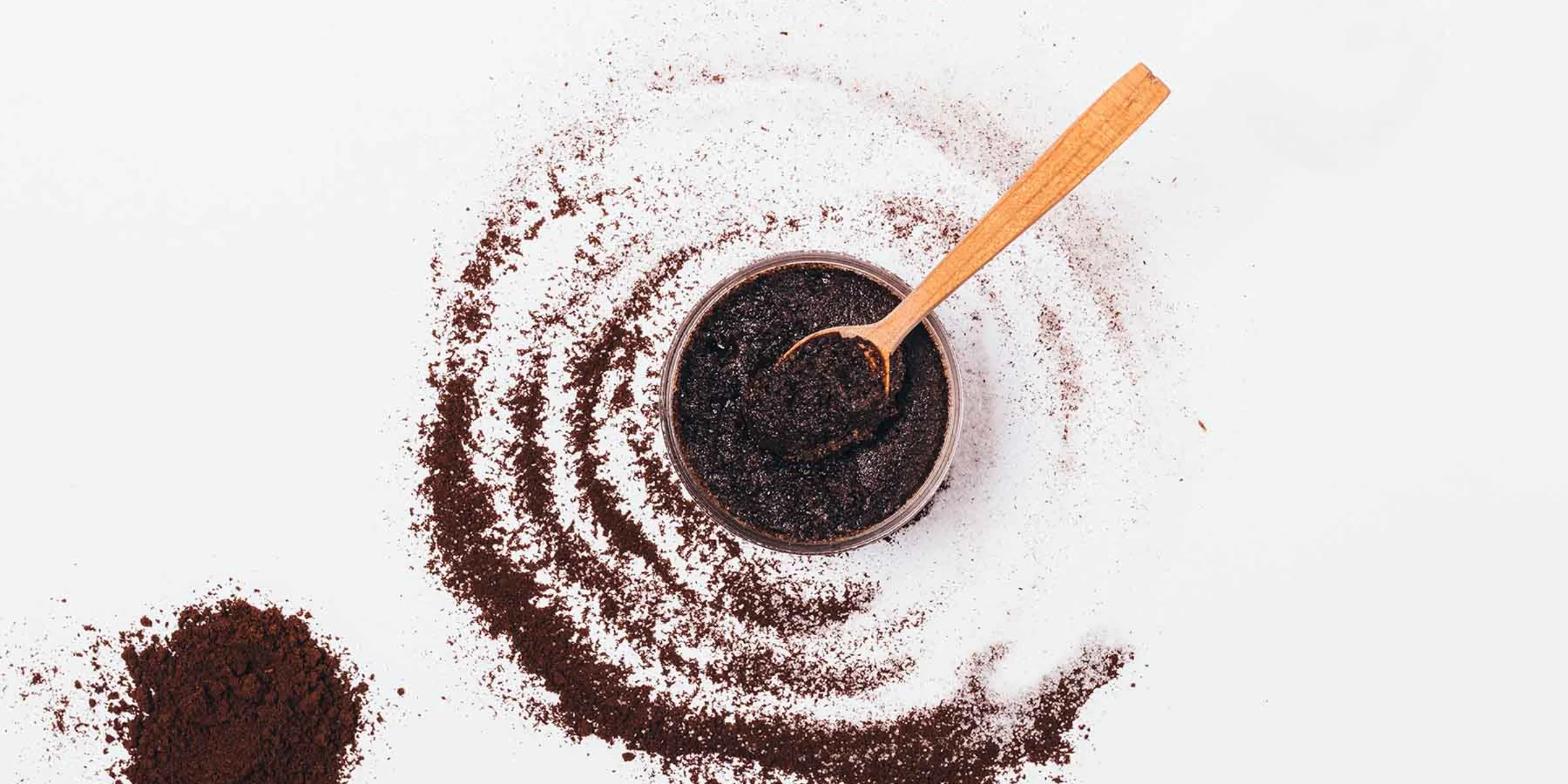 Ciotola con polvere di caffè e cucchiaio di legno, circondata da polvere di caffè sparsa.