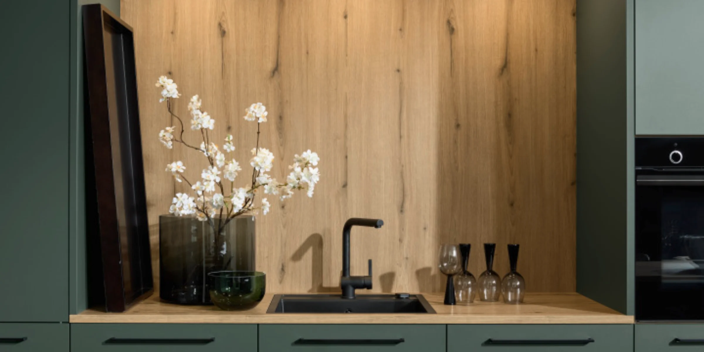 Cucina moderna con accenti in legno e armadi verdi di Nolte Kitchen.