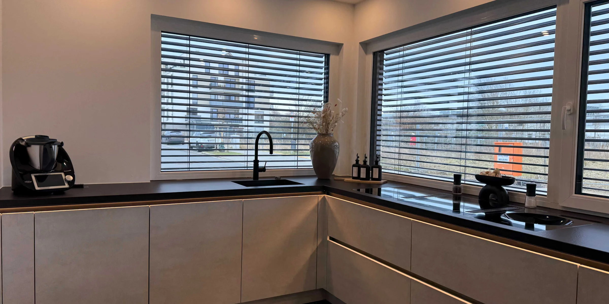 Modern kitchen with large windows and dark countertops. Nolte Kitchen.