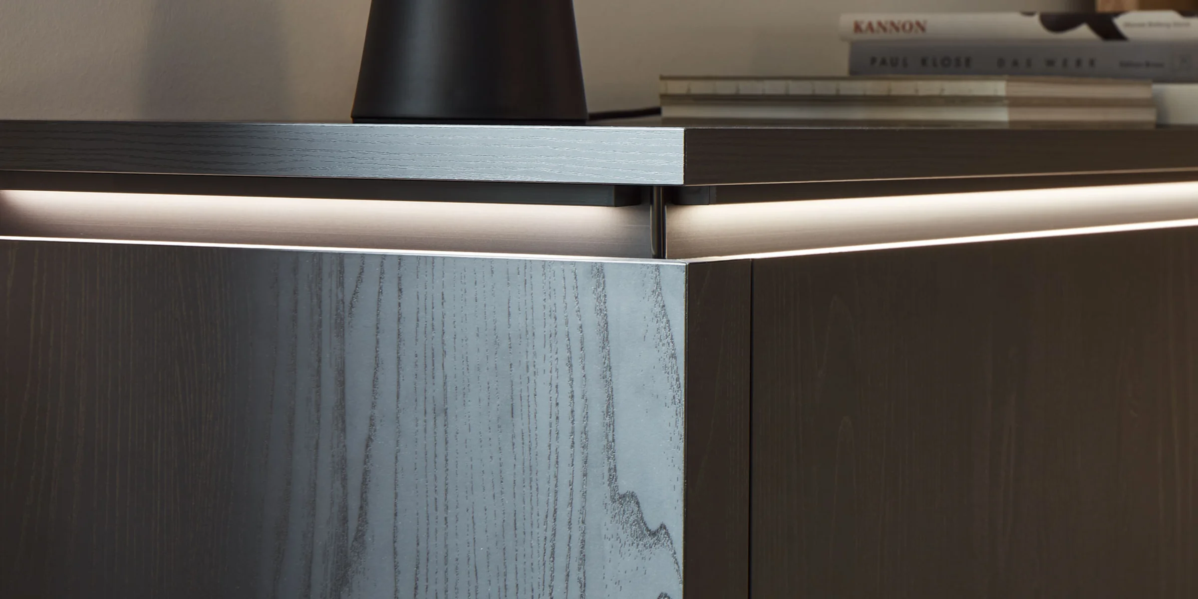 Moderno sideboard in legno scuro con illuminazione, libri e decorazioni sopra, di Nolte Living.