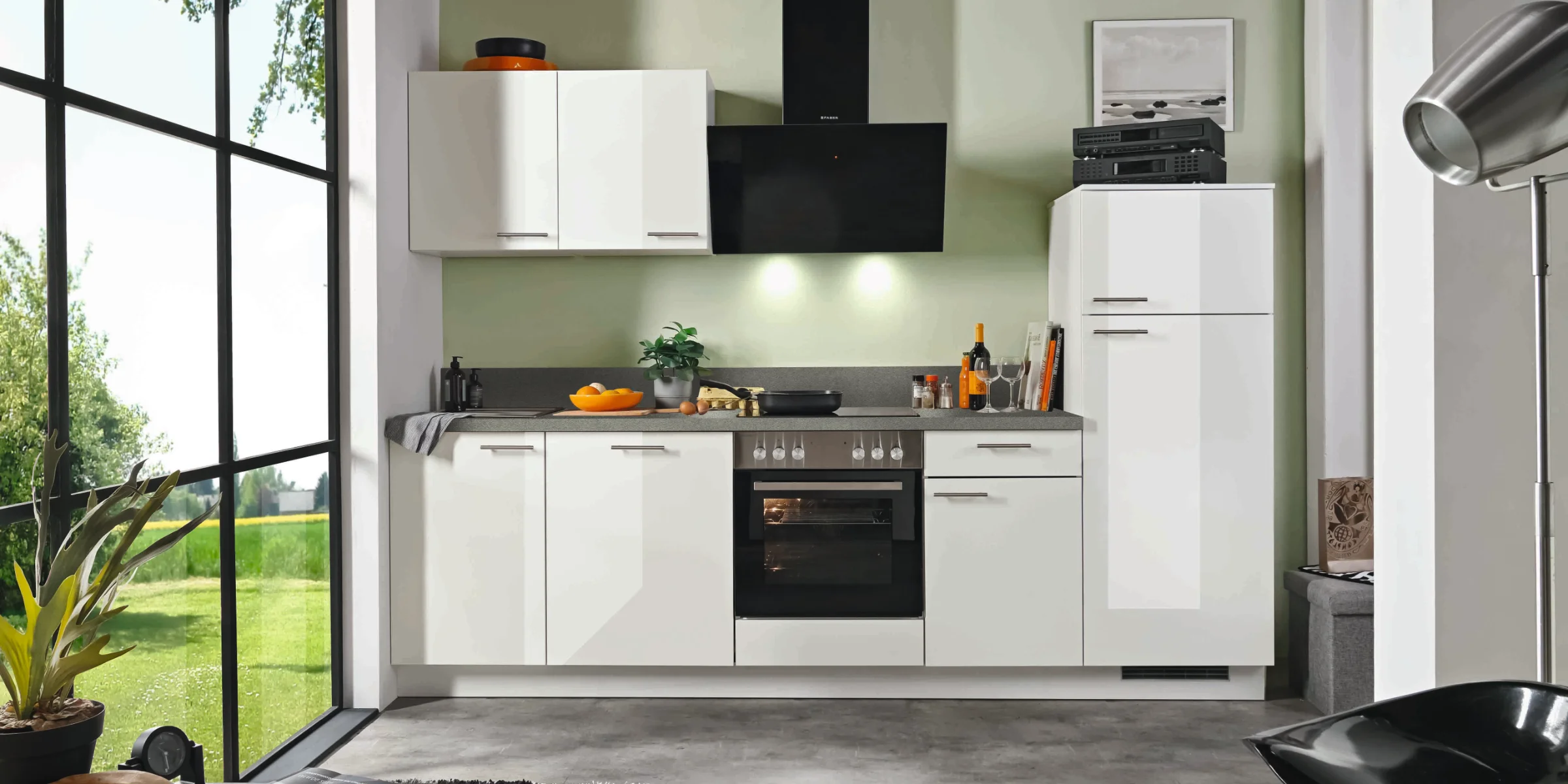 Dans la cuisine moderne d'Express Küchen, des armoires blanches et une cuisinière se trouvent devant un mur vert.