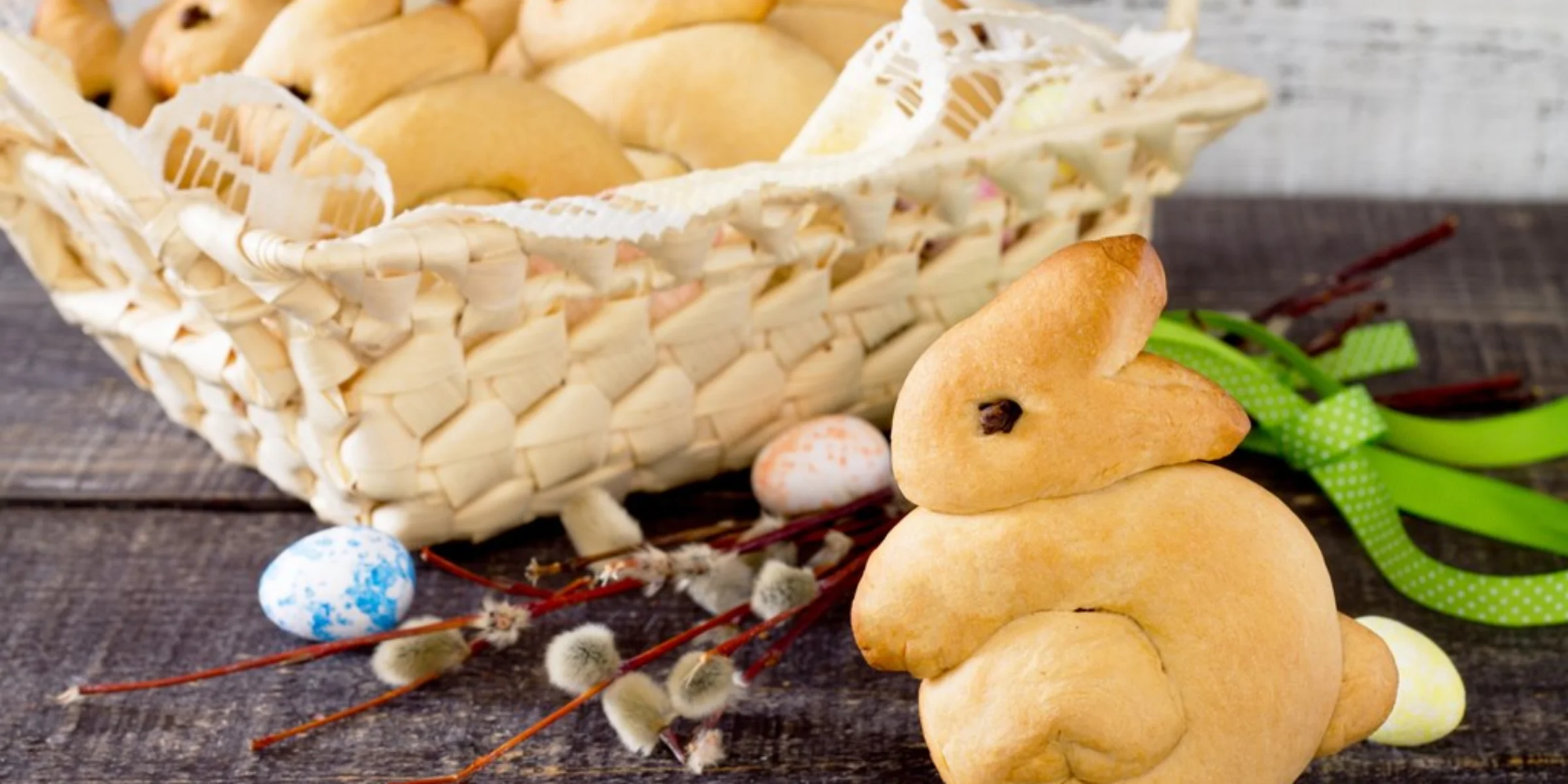 Un cesto pasquale con coniglietti di pane e uova dipinte su un tavolo di legno.