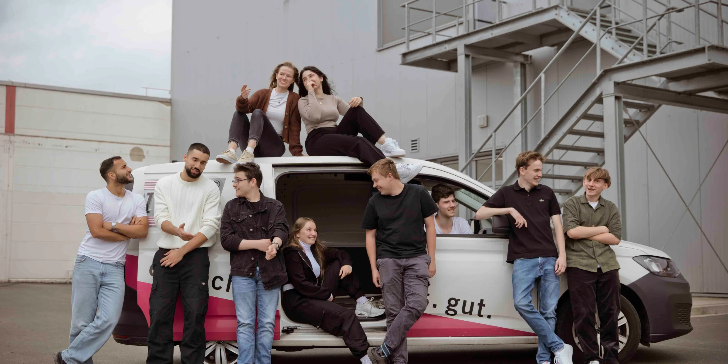 Eine Gruppe Jugendlicher posiert lässig auf und neben einem Auto im Freien.