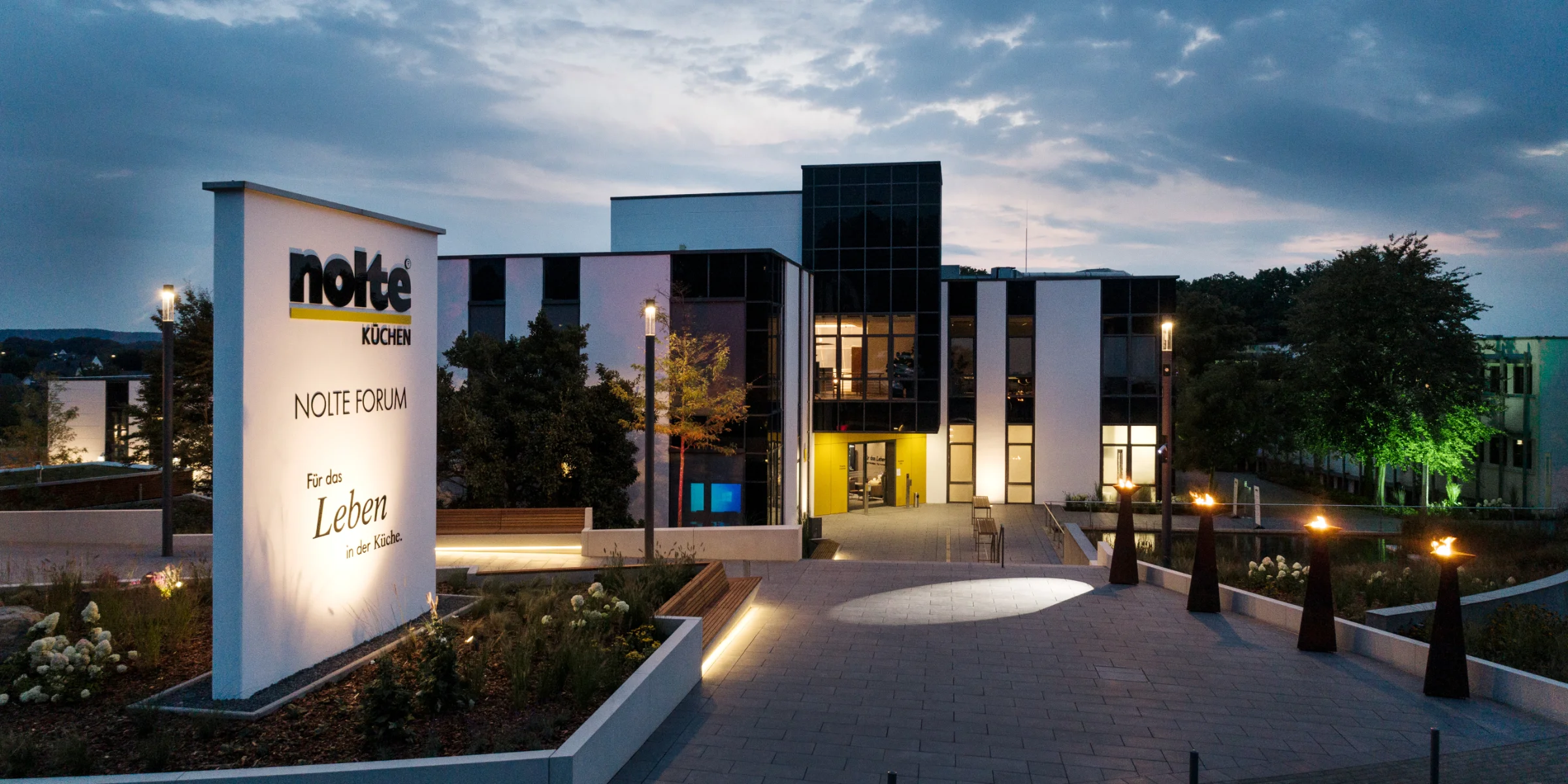 Edificio moderno al crepuscolo con insegna illuminata di Nolte Kitchen in primo piano.