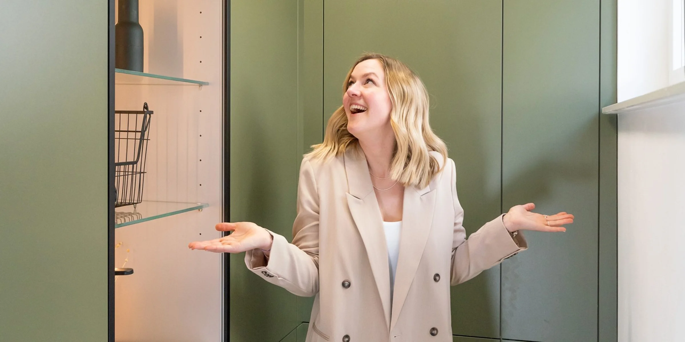 Una donna in una moderna lavanderia con armadi verdi di Nolte Utility Rooms.