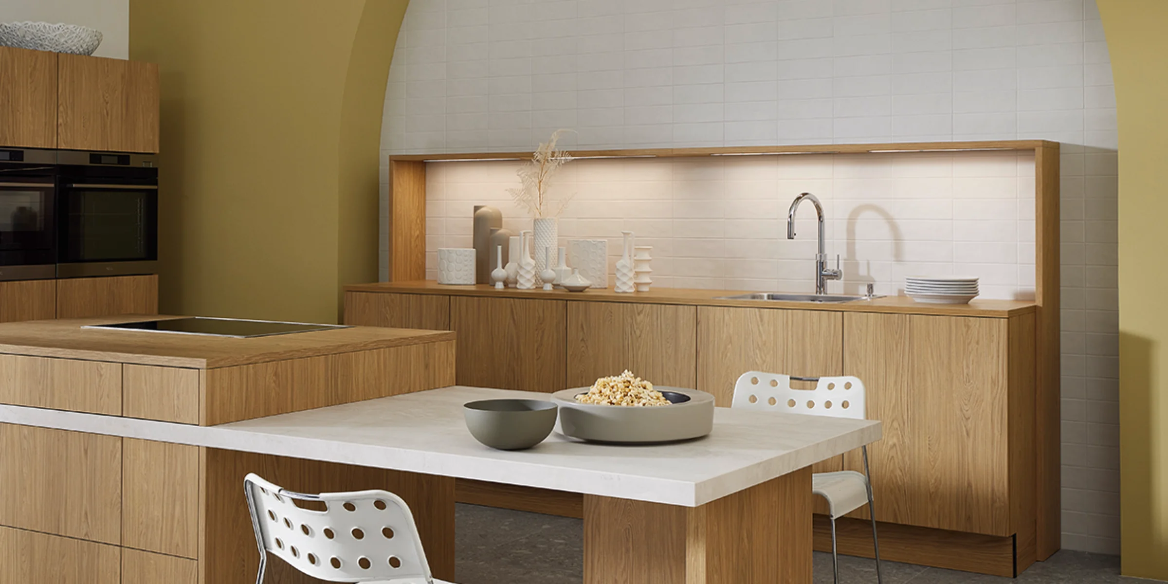 Cucina moderna con frontali in legno e zona pranzo integrata davanti a parete gialla. Nolte Kitchen.
