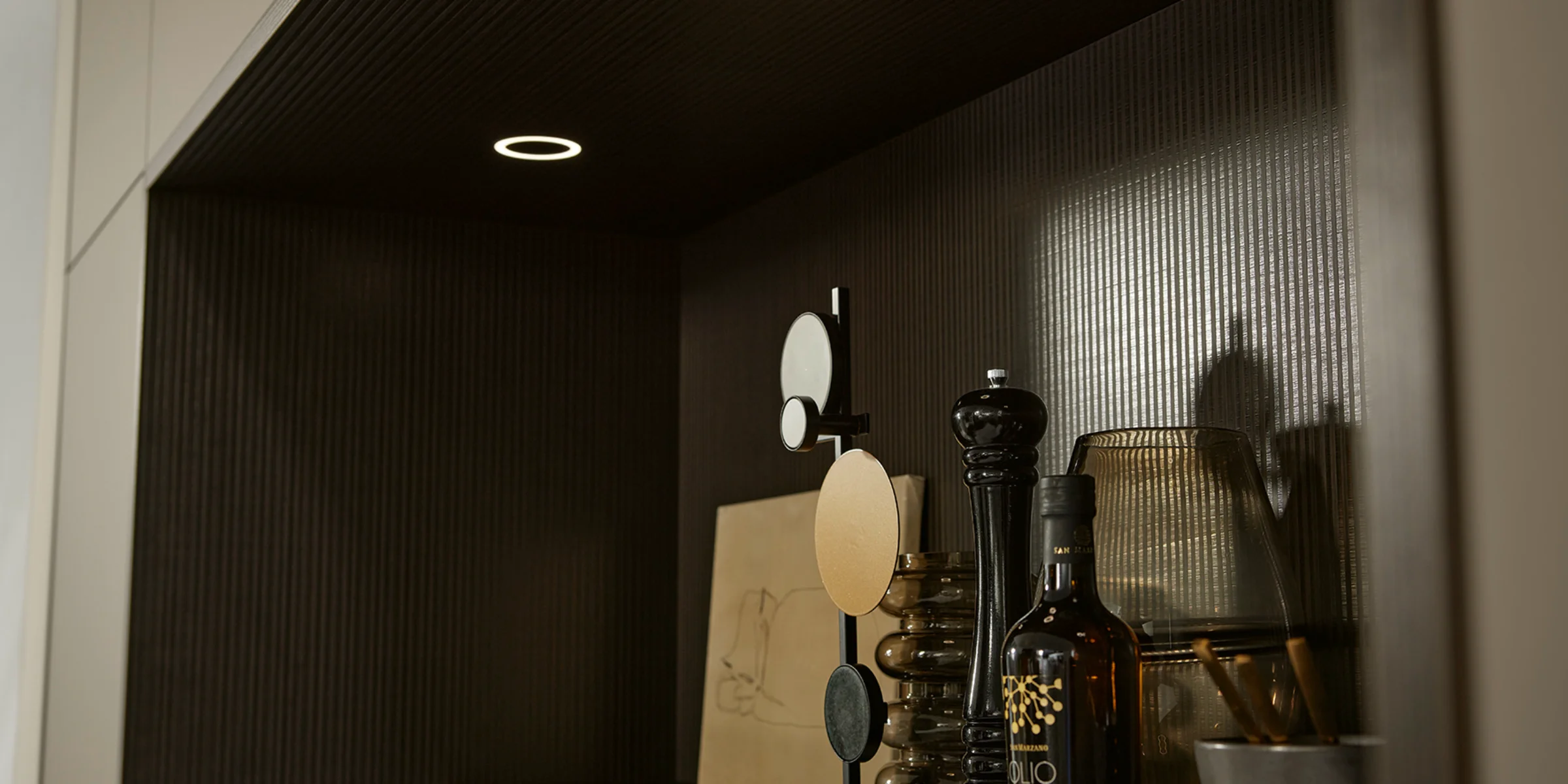 Scaffale con spezie e decorazioni, illuminato da faretti incassati. Nolte Cucine.