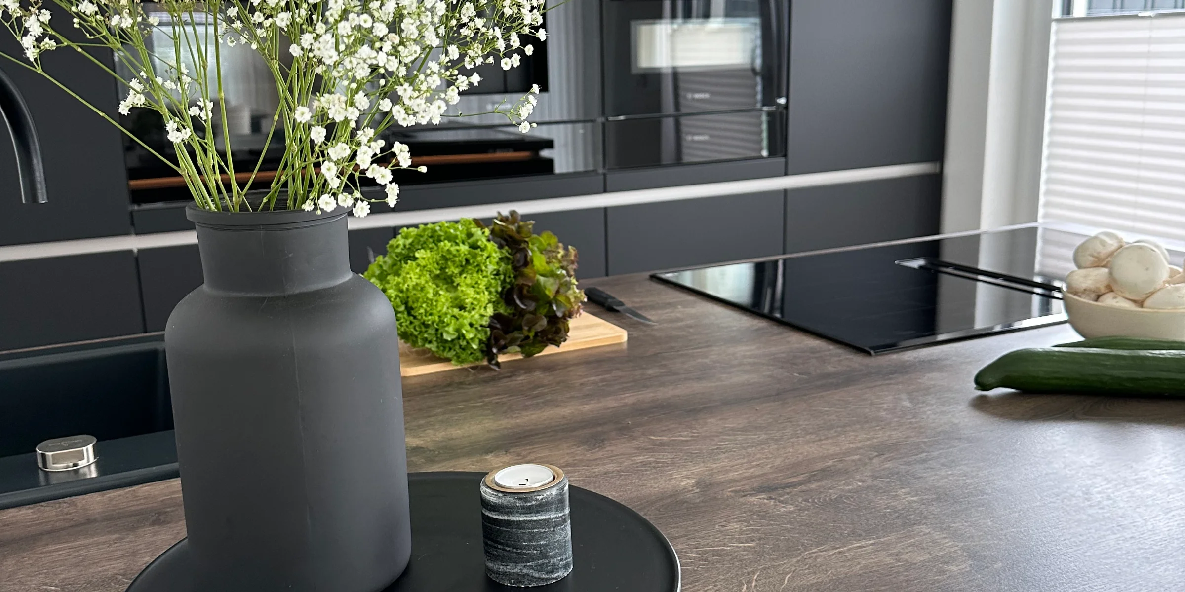 In una cucina moderna con armadi scuri, un vaso di fiori è sul piano di lavoro. Nolte Kitchen.