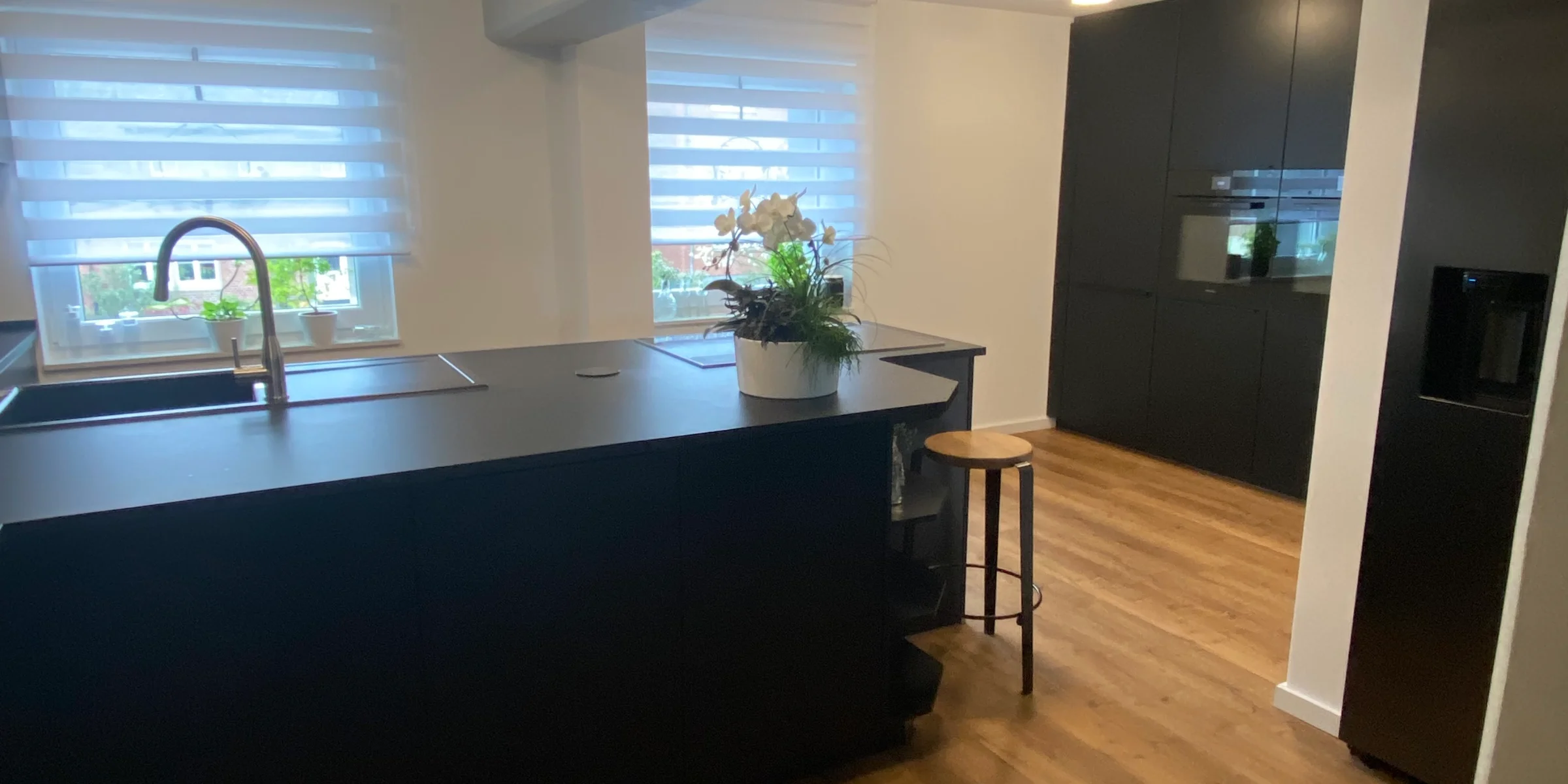 Cucina moderna con armadi scuri e pavimento in legno, arredata da Nolte Kitchen.