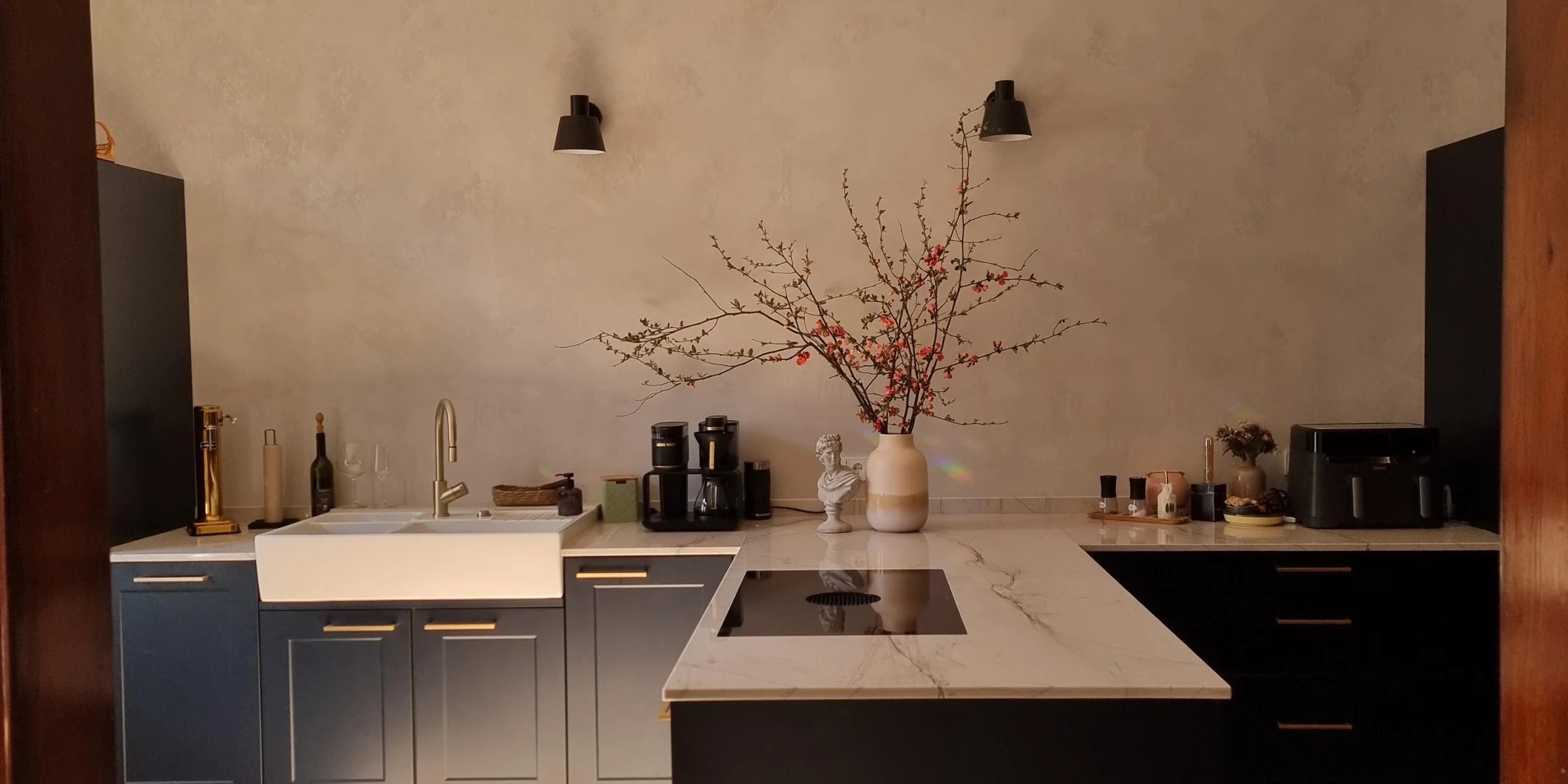 Cucina moderna con isola e armadi scuri, illuminata da un lampadario. Nolte Kitchen.