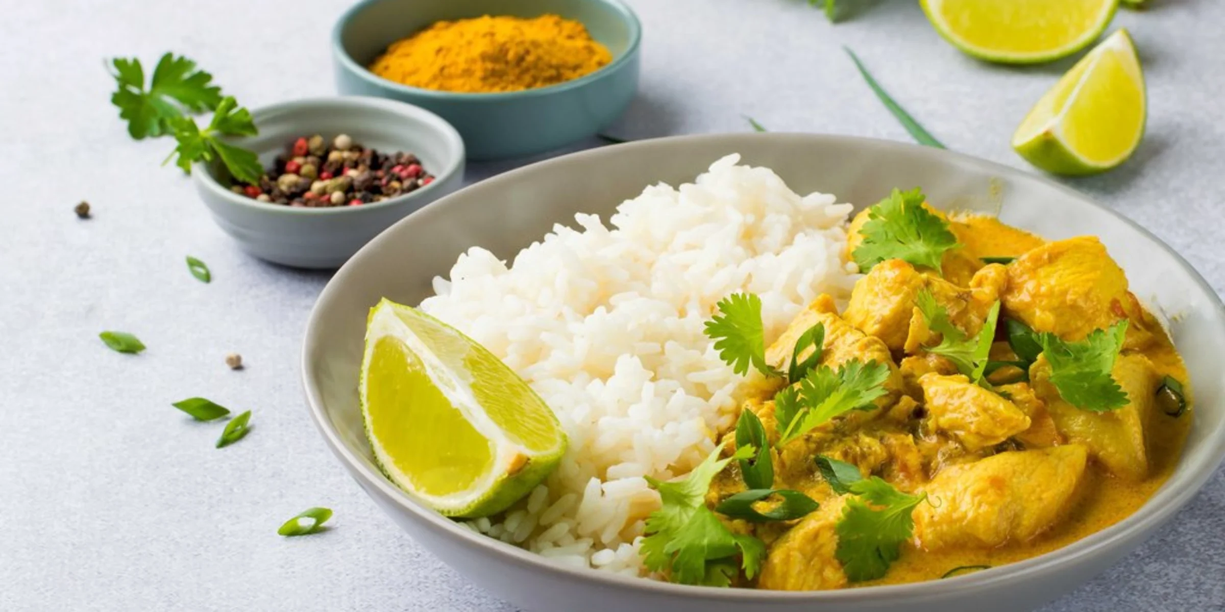 Ciotola di pollo al curry con riso, lime e coriandolo su un tavolo.