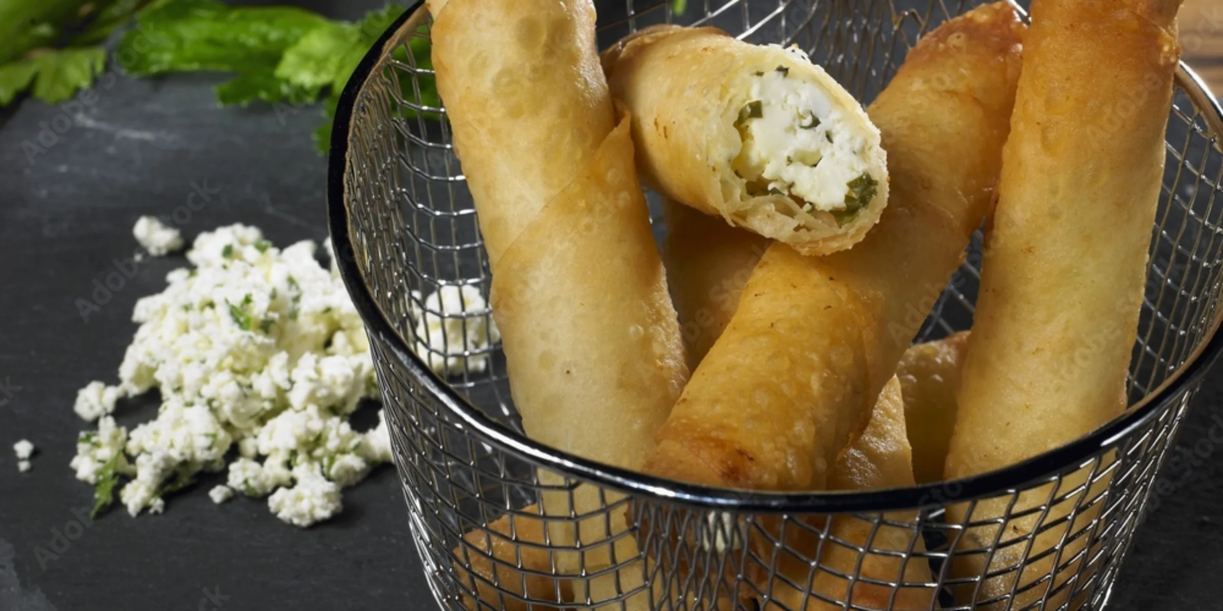 Involtini croccanti al formaggio su ardesia, decorati con erbe fresche.