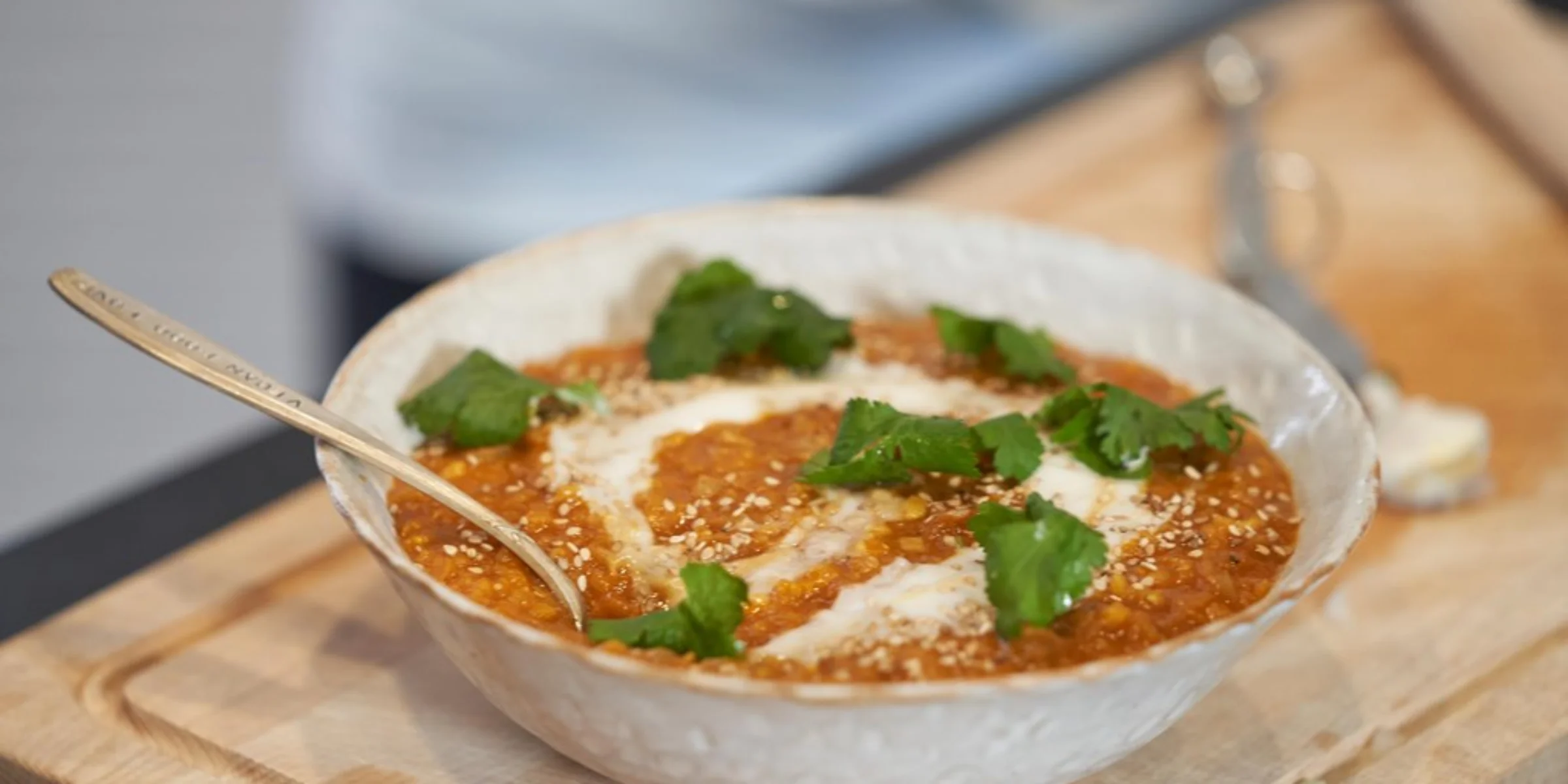 Ciotola di zuppa di lenticchie con panna e coriandolo su tagliere di legno.