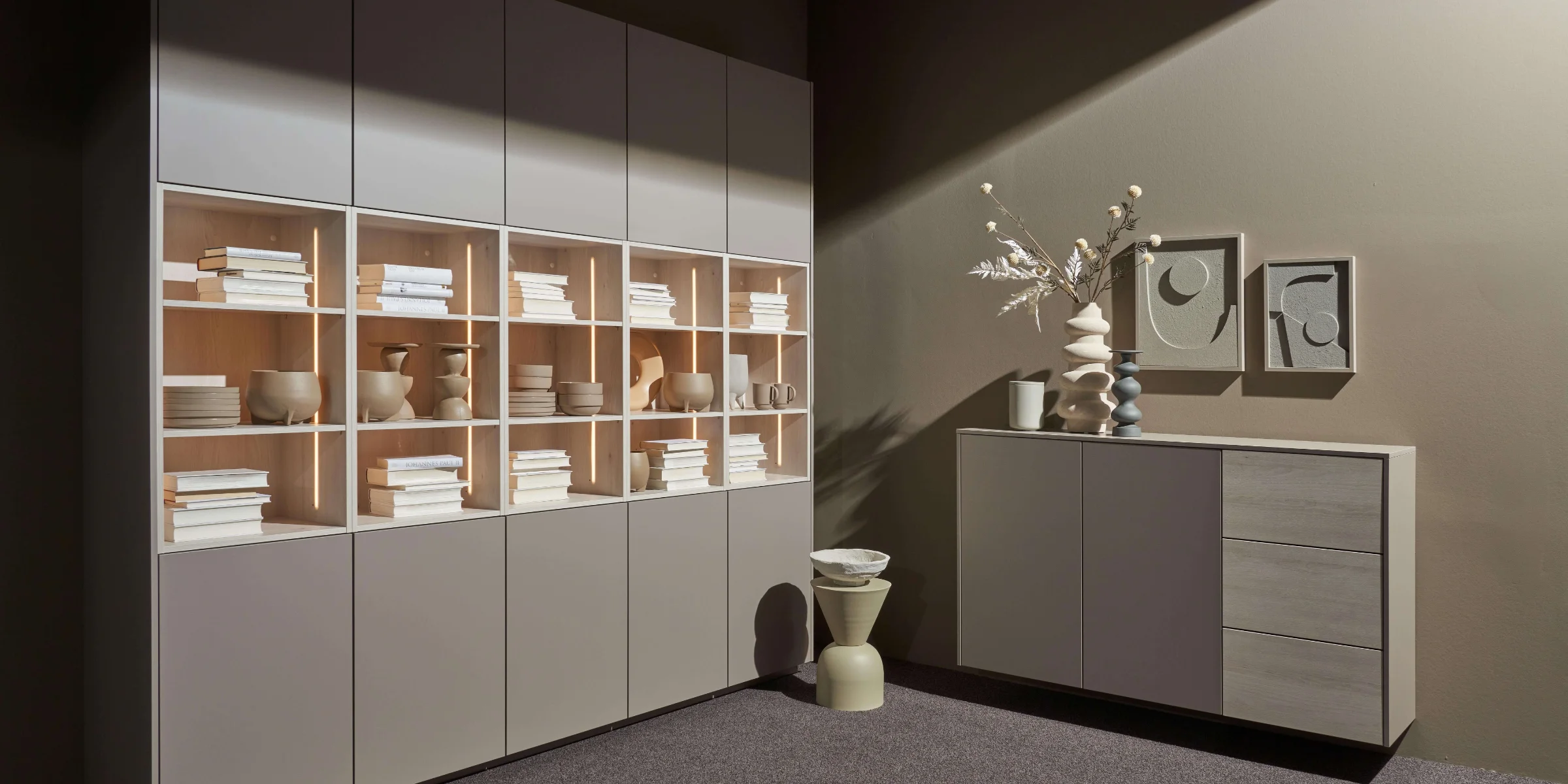 Soggiorno con scaffali e credenza moderni, decorati con vasi e libri, di Nolte Living.