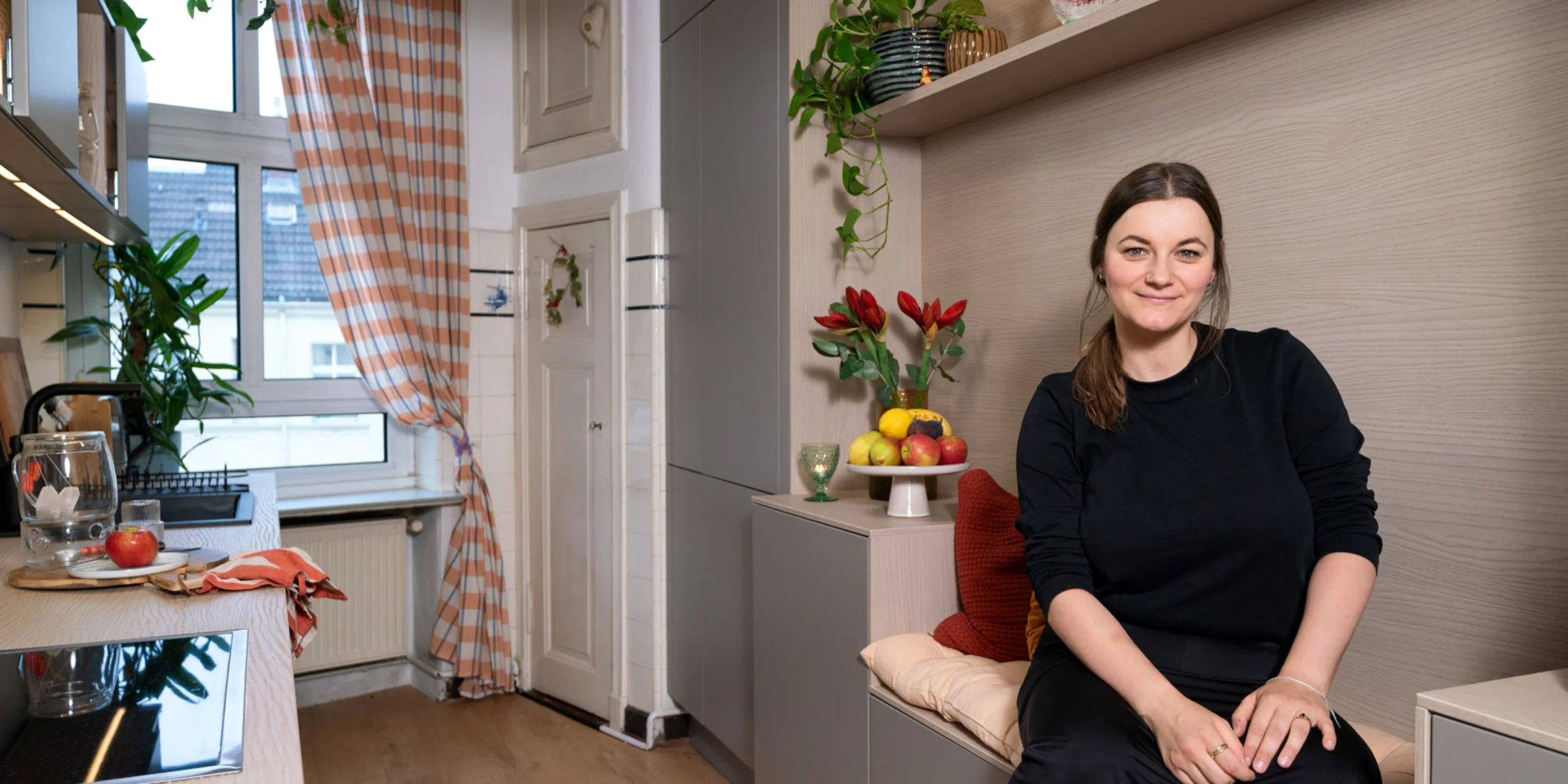 Una donna siede in una cucina moderna con piante, design di Nolte Kitchen.