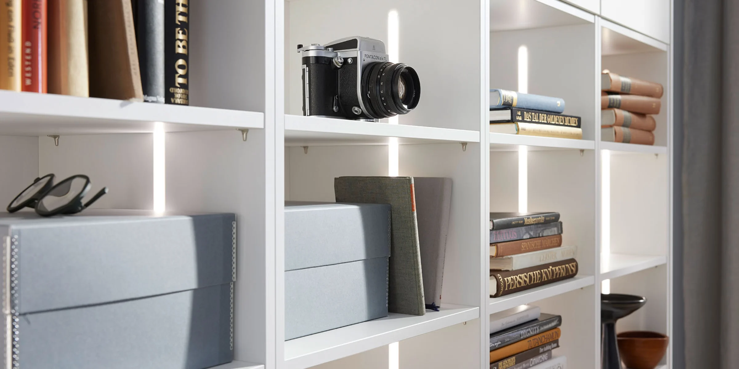 Scaffale con libri, fotocamera e scatole; esempio di elegante stoccaggio di Nolte Living.