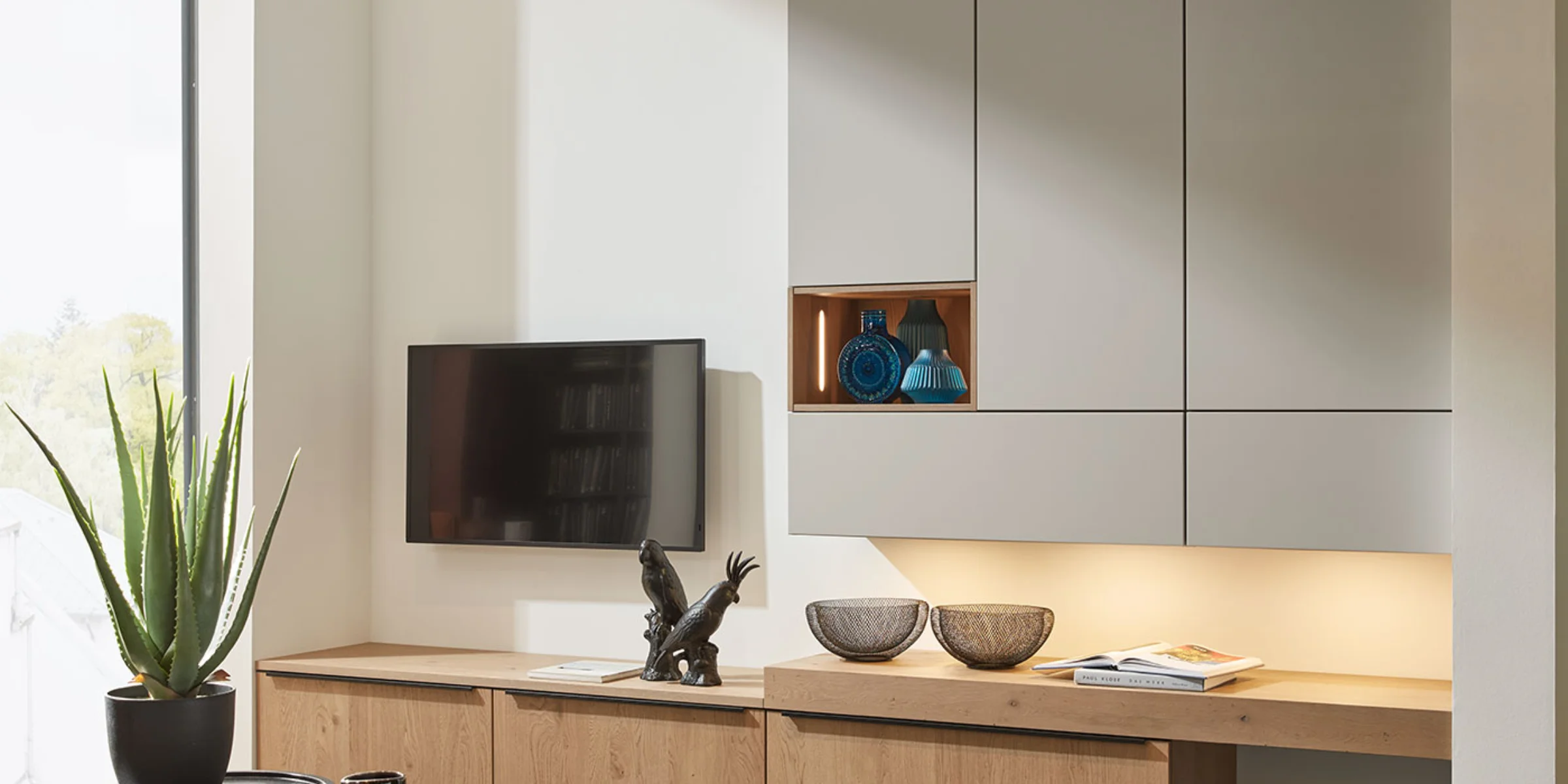 Soggiorno moderno con eleganti armadi e TV, decorato con piante e sculture, Nolte Living.
