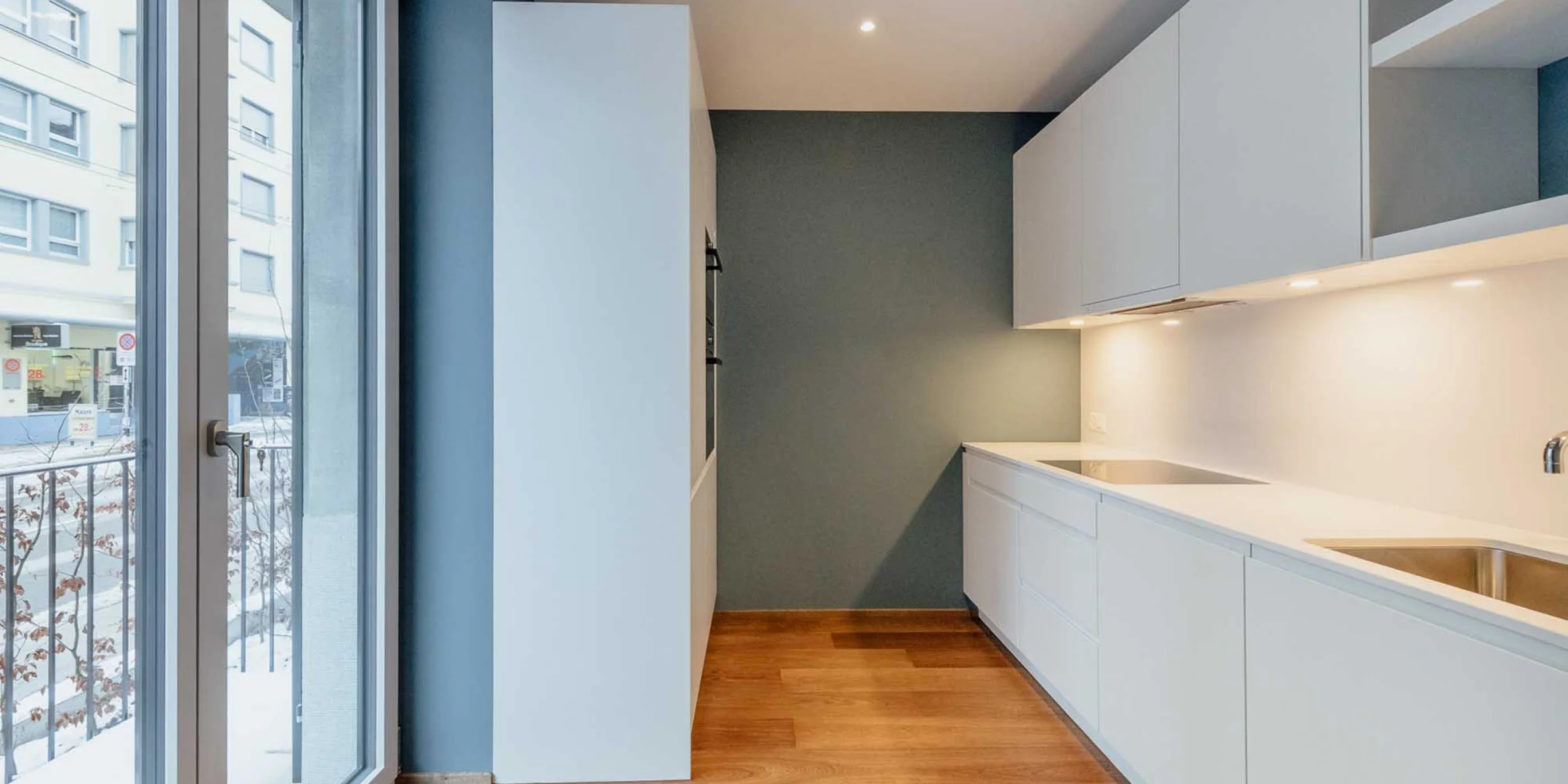 Cucina moderna con armadi bianchi e pavimento in legno, progettata da Nolte Kitchen.