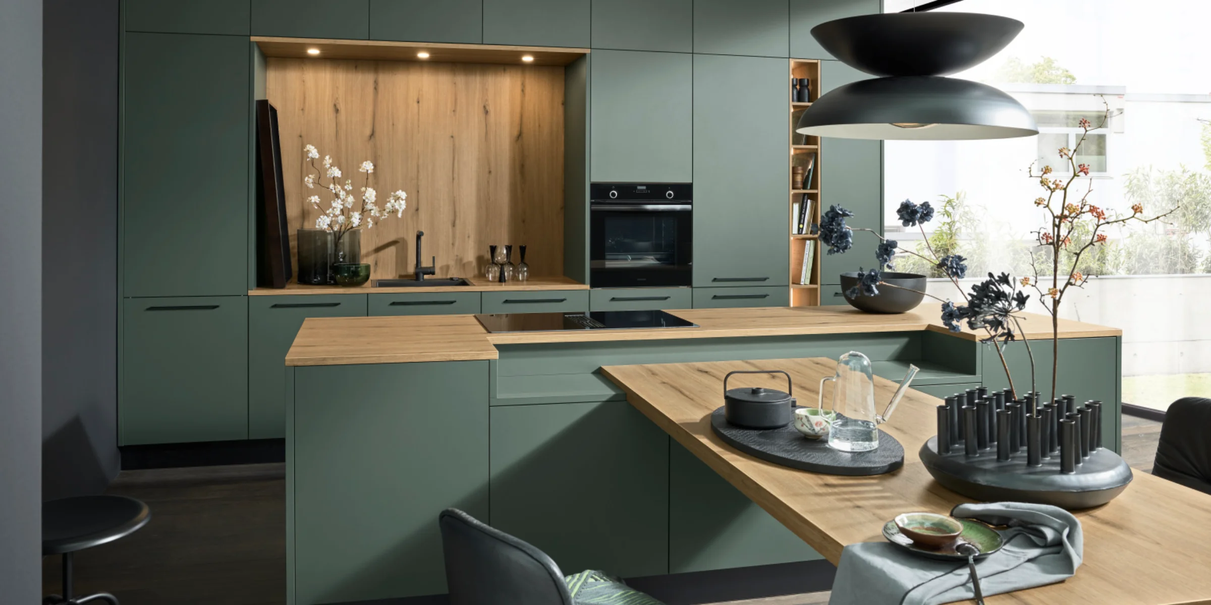 Una cucina moderna verde con accenti in legno e illuminazione elegante. Nolte Kitchen.