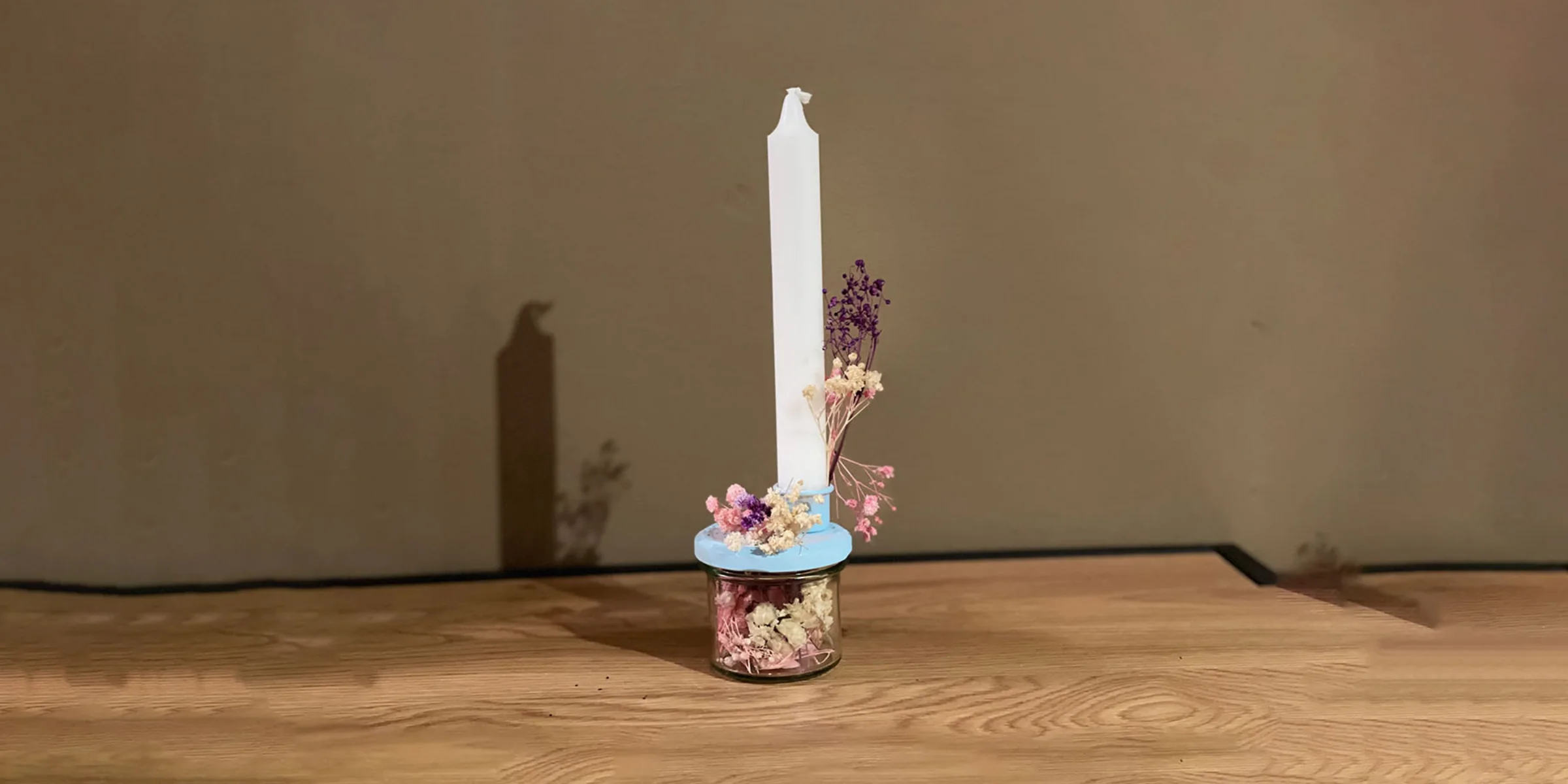 Una singola candela accesa su un tavolo di legno decorato con fiori secchi.