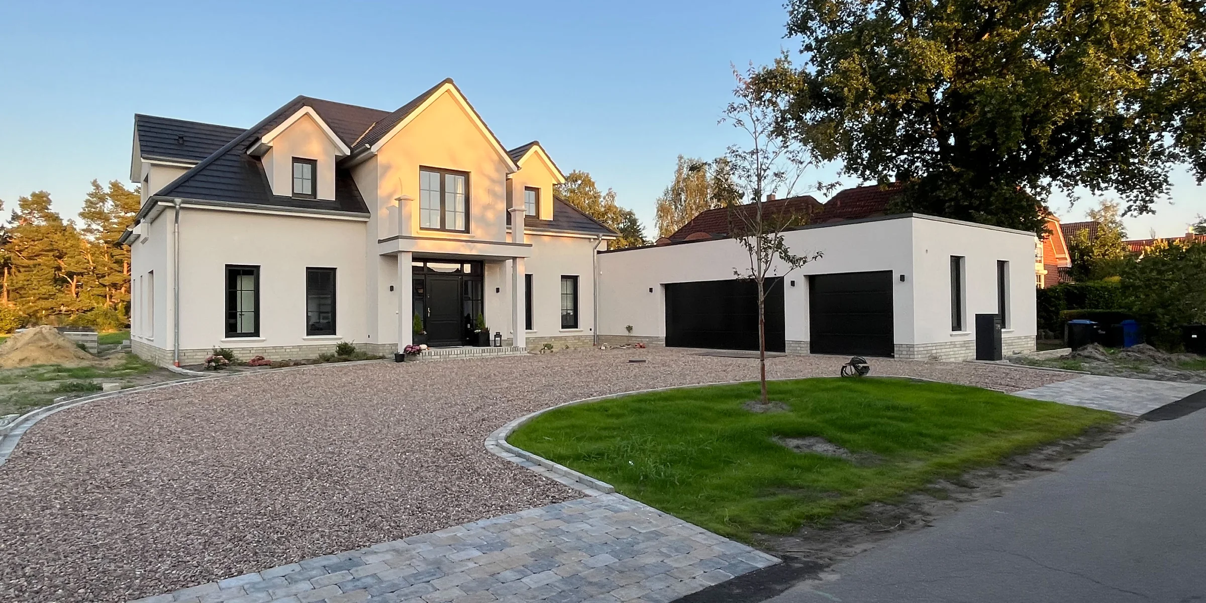 Modern home with large front yard and paved driveway at sunset.