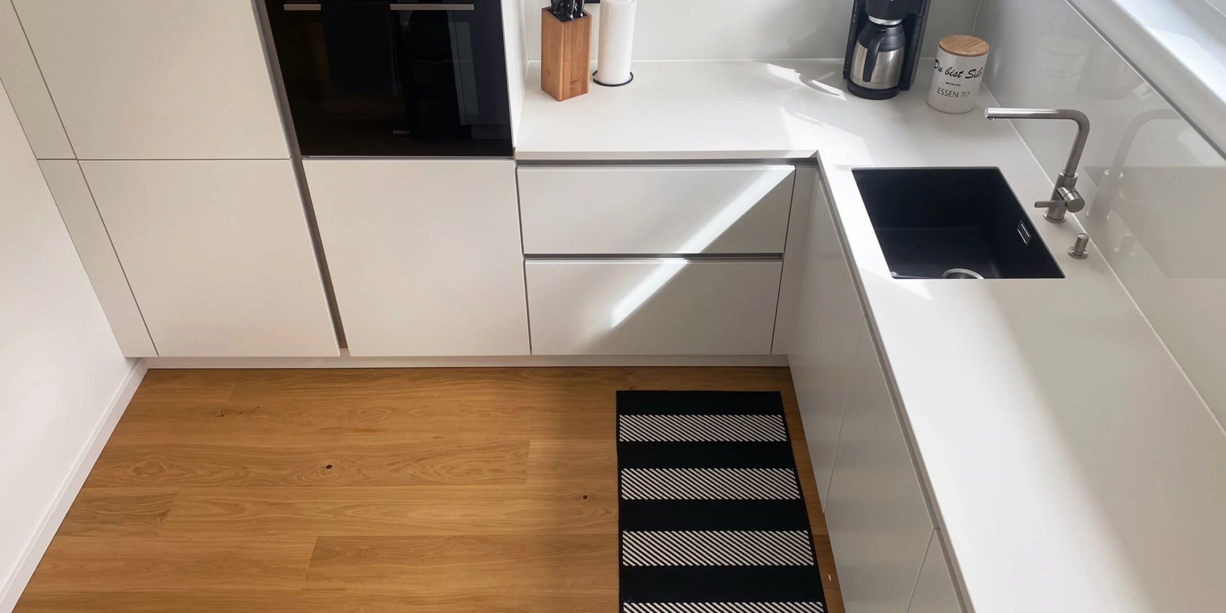 Cucina moderna con armadi bianchi e pavimento in legno, Nolte Kitchen.