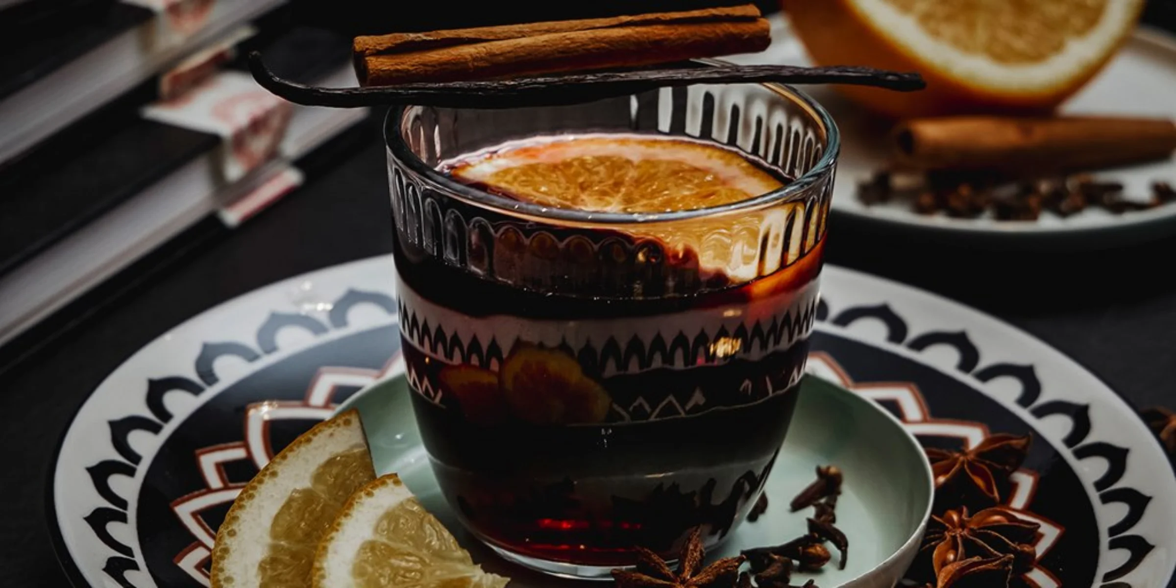 Bevanda calda con fette di agrumi e bastoncino di cannella su un piatto decorativo.