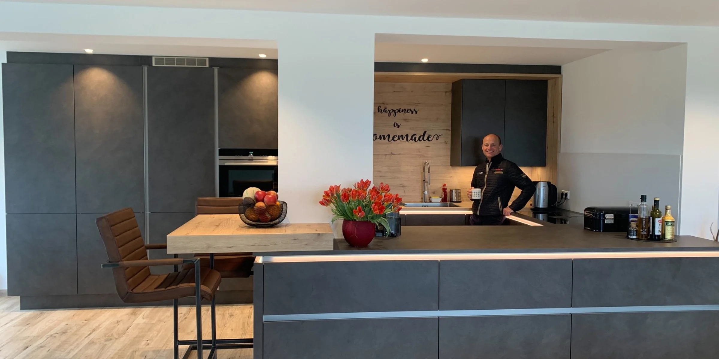 Cucina moderna con armadi scuri e una persona al bancone. Nolte Kitchen.