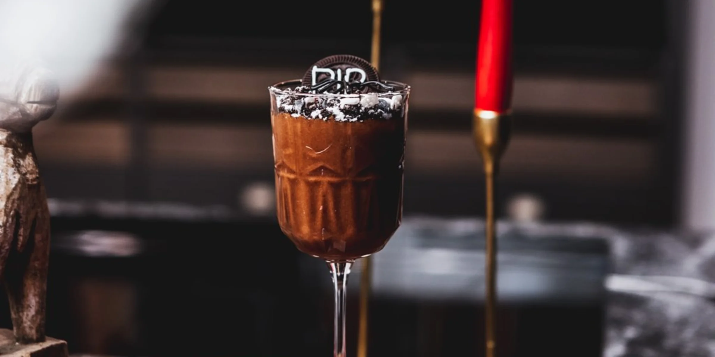Un bicchiere di mousse al cioccolato con biscotti su un tavolo, sullo sfondo candele rosse.
