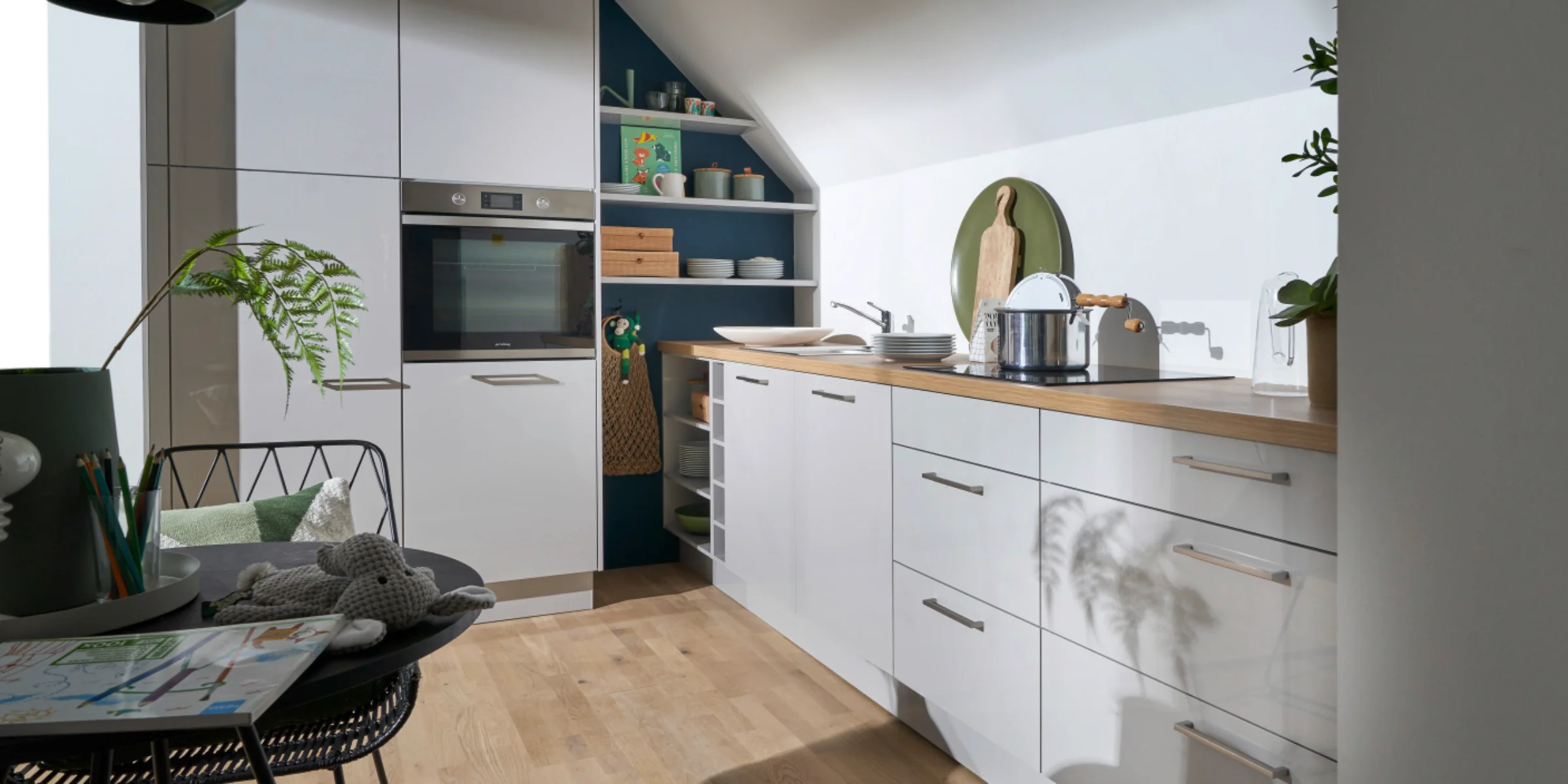Cucina moderna con armadi bianchi e piano in legno sotto un tetto spiovente. Nolte Kitchen.
