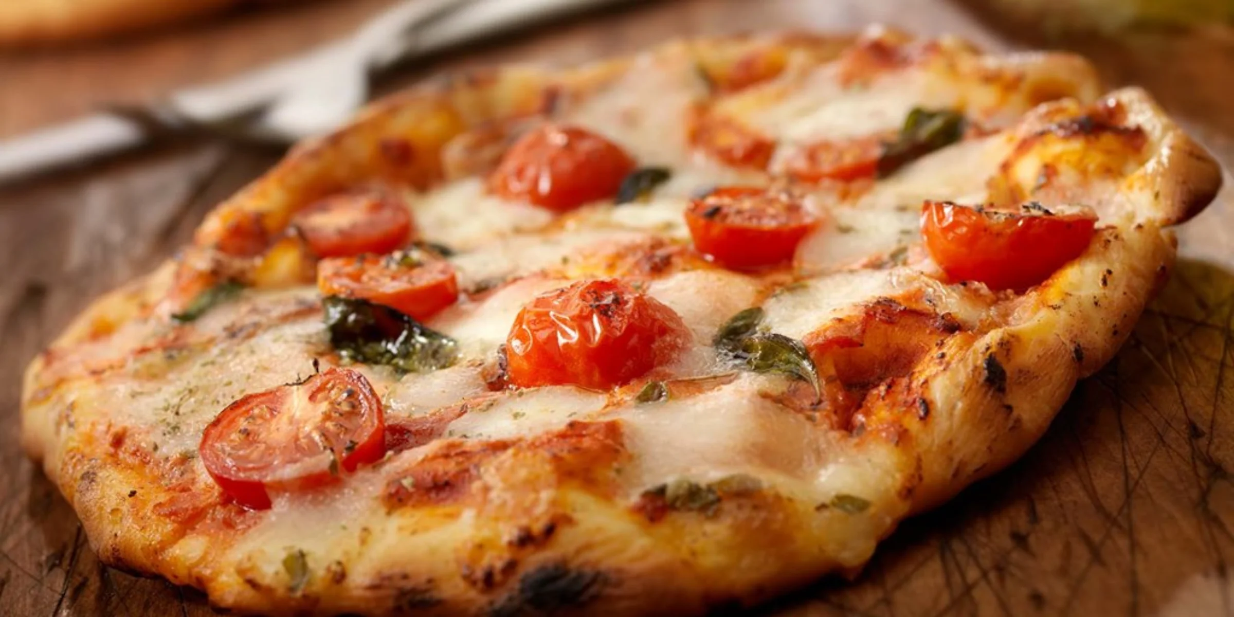 Pizza appena sfornata con pomodori e basilico su un tagliere di legno.