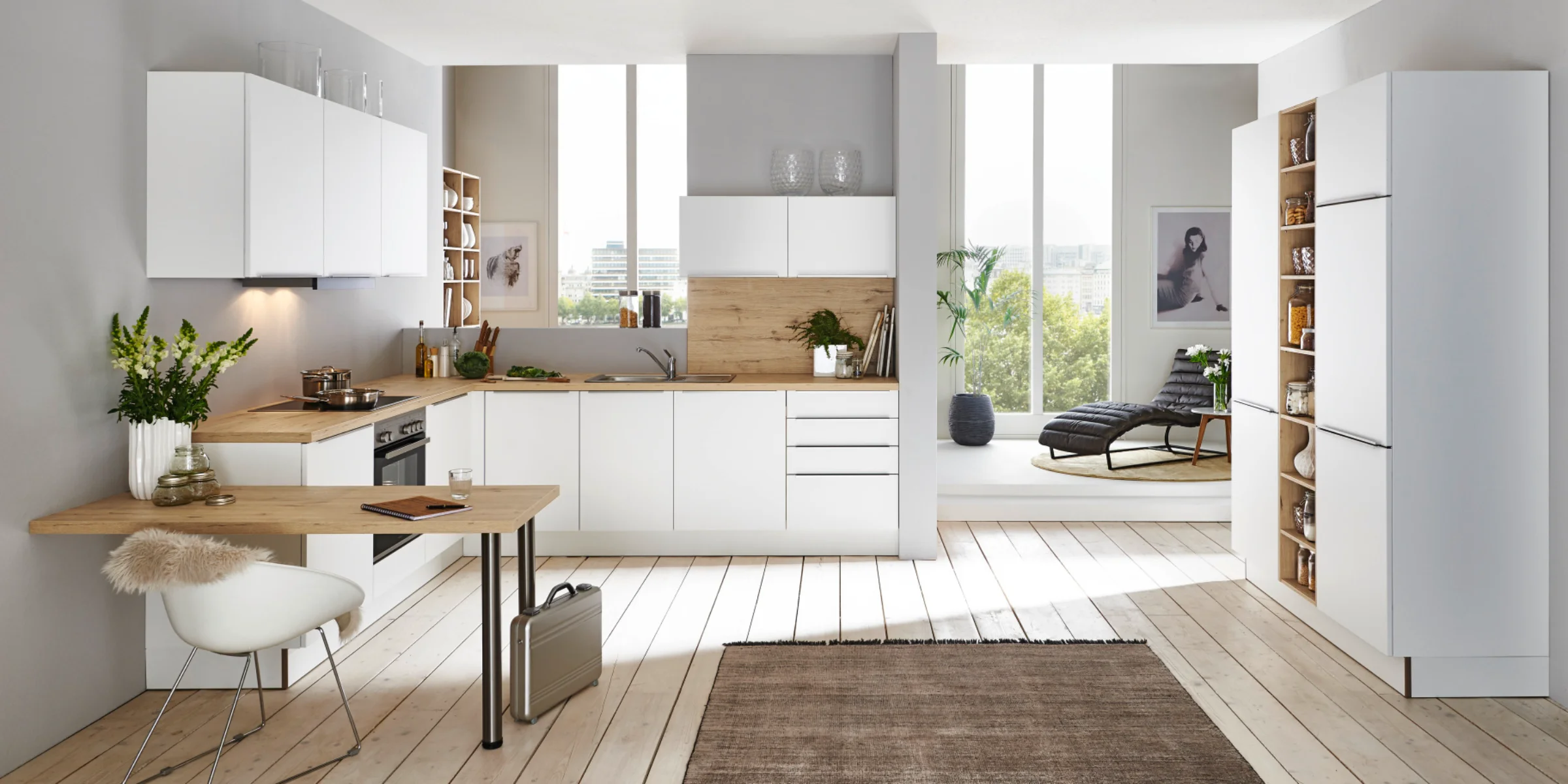 Helle Nolte cucina con il programma di frontali PLUS in bianco softmatt, combinato con piani di lavoro in legno e postazione di lavoro integrata in ambiente living aperto e pieno di luce.
