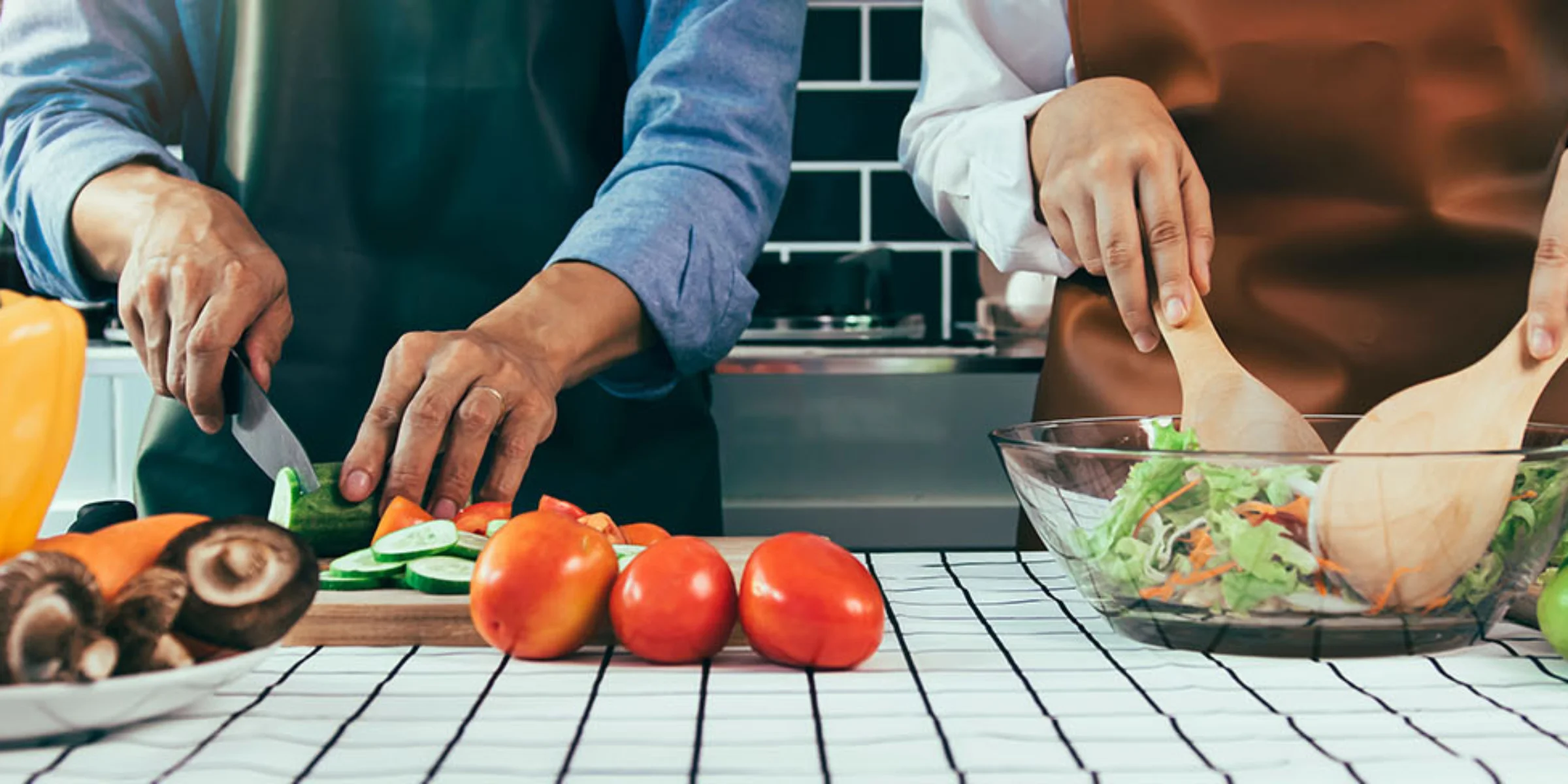 Due persone preparano insieme un pasto. Sul piano di lavoro della cucina vengono tagliate verdure e mescolata un'insalata.