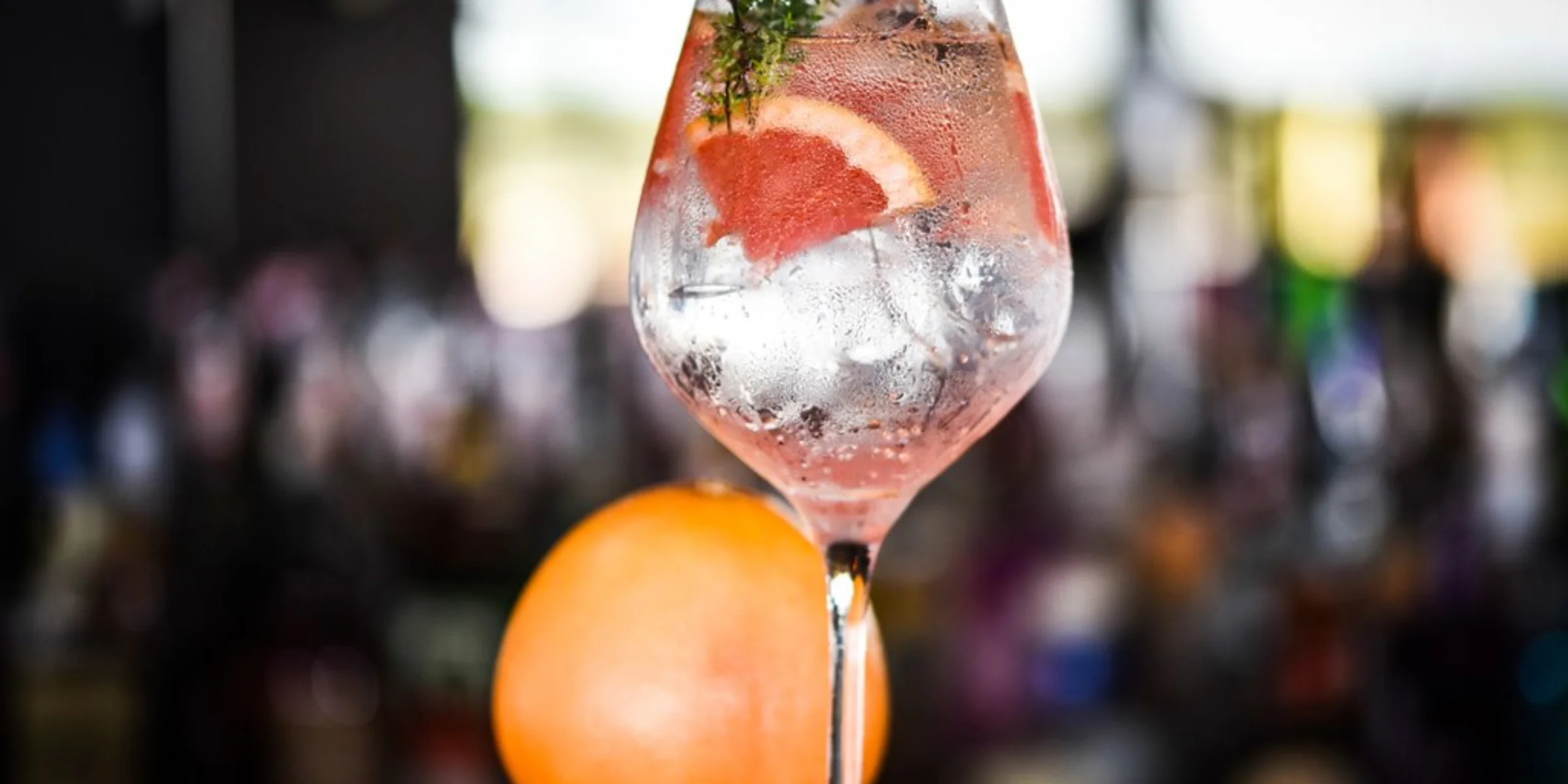 Bicchiere da cocktail con ghiaccio, rametto di timo e fetta di pompelmo su un bancone.