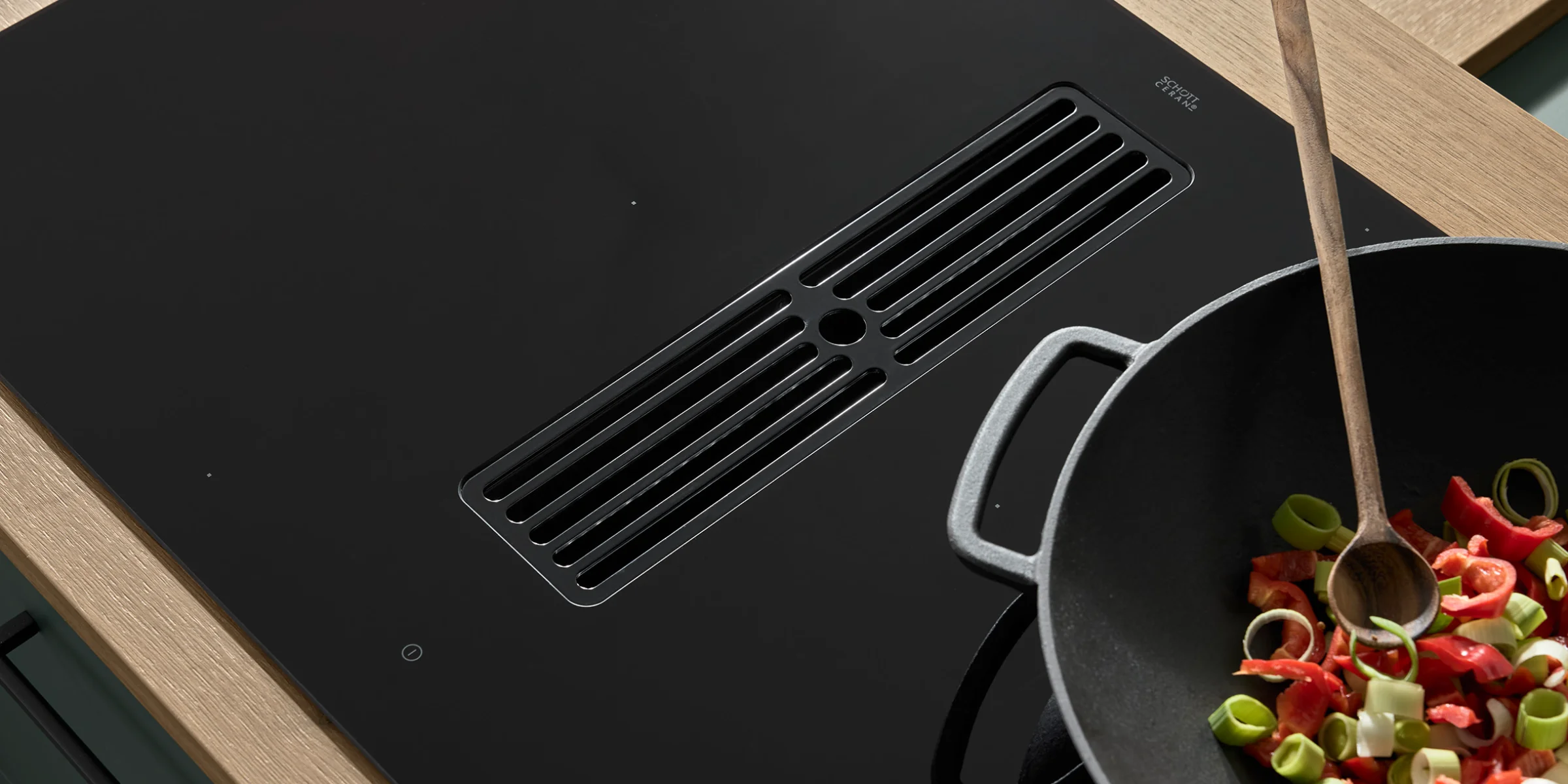 Un moderno piano cottura con aspiratore, wok e verdure in una cucina Nolte.